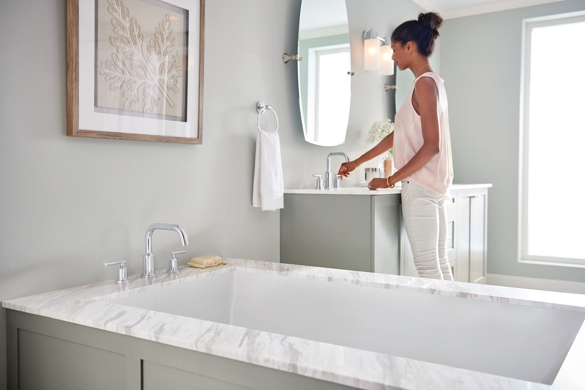 Chrome two-handle roman tub faucet with modern design mounted on marble deck rim above soaking tub.