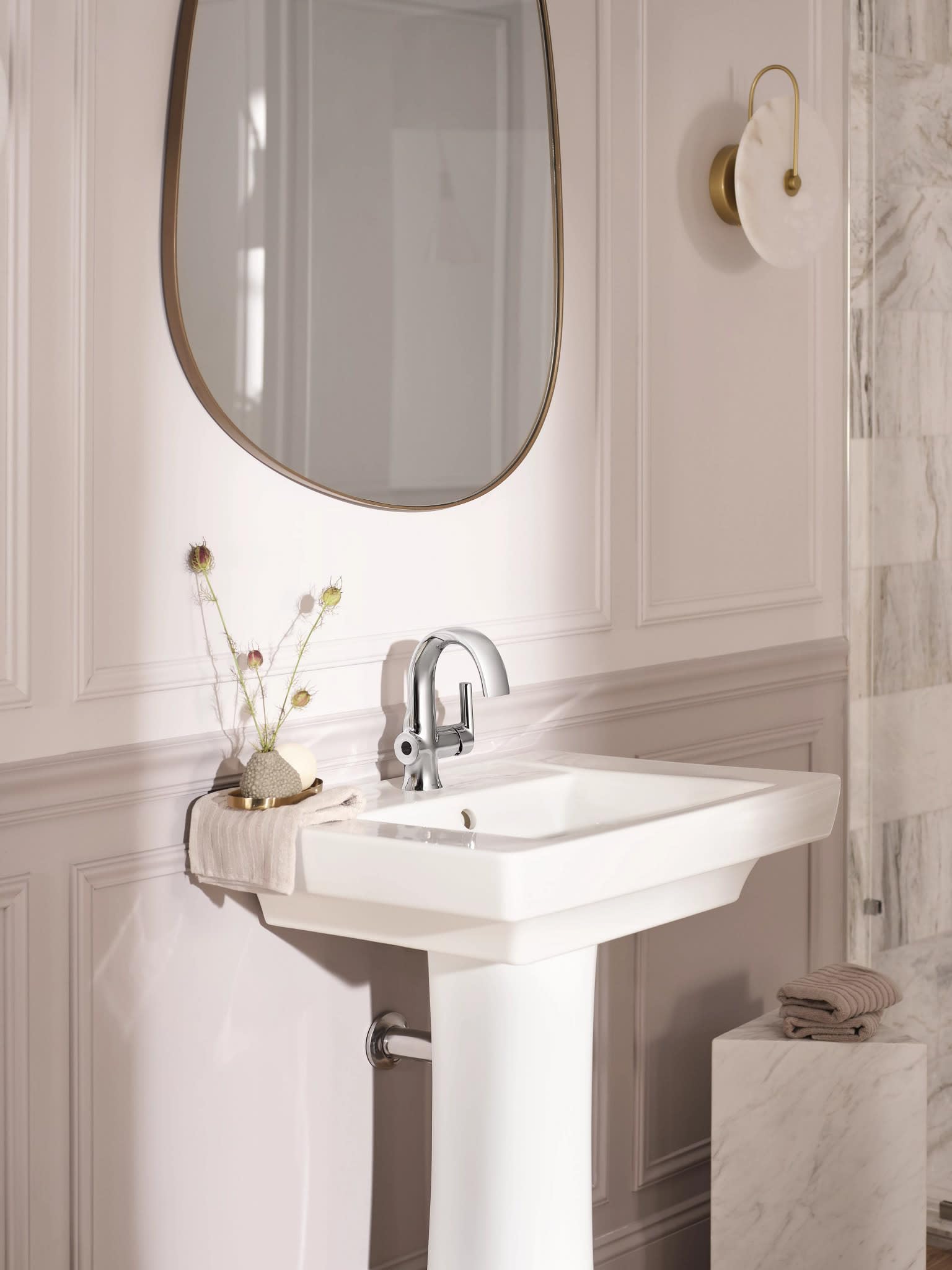 Chrome single-handle bathroom sink faucet with curved spout mounted on white pedestal sink.