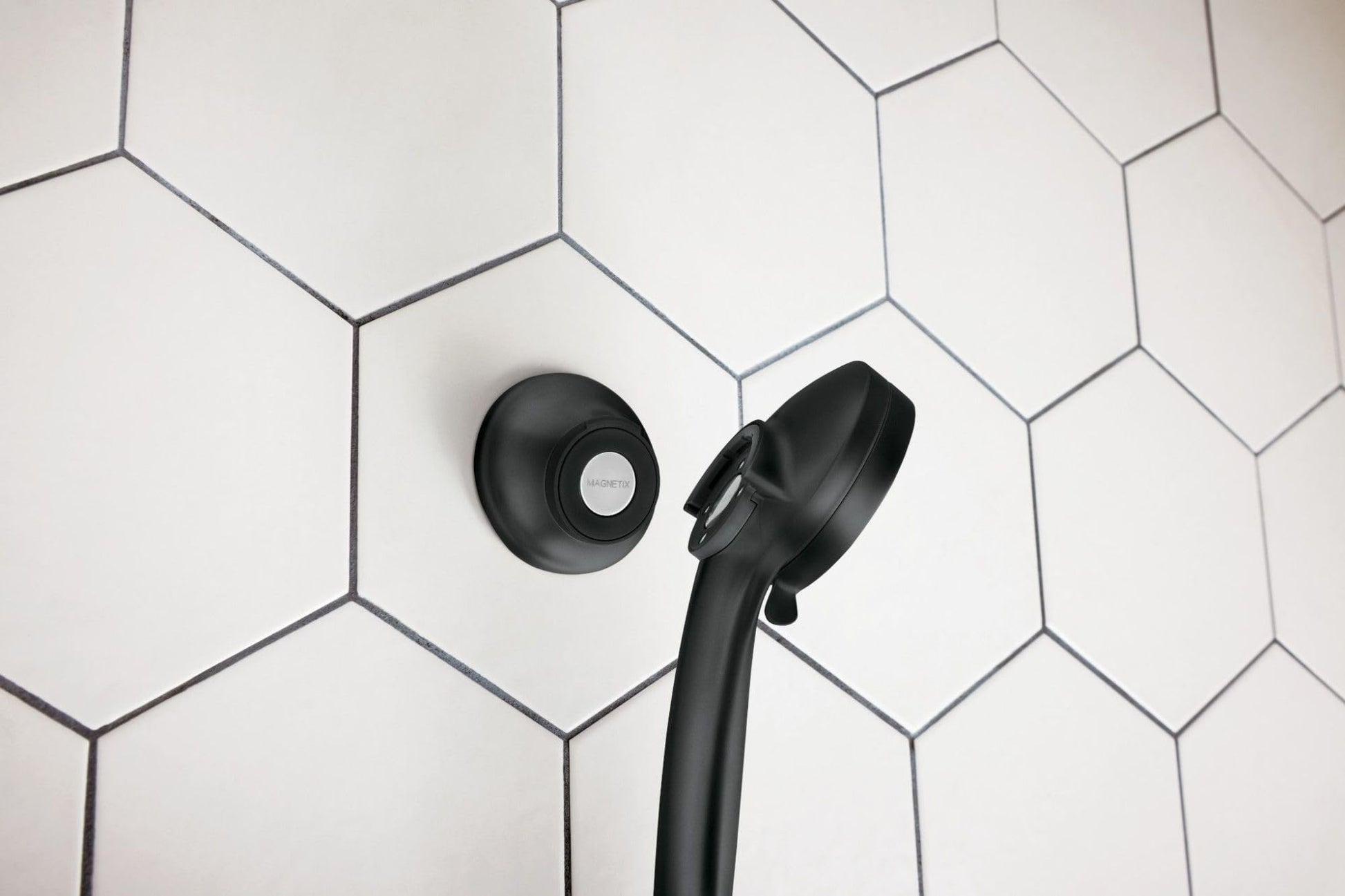 Matte black circular magnetic dock mounted on white hexagonal tile wall with black showerhead positioned in dock.