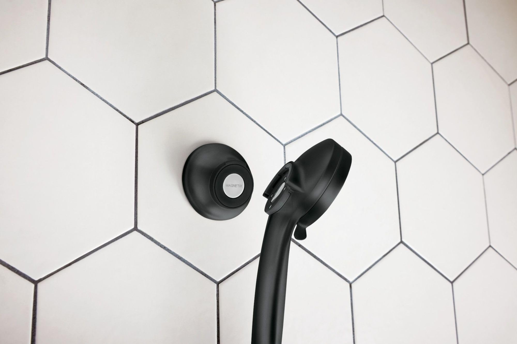 Matte black circular magnetic dock mounted on white hexagonal tile wall with black showerhead positioned in dock.