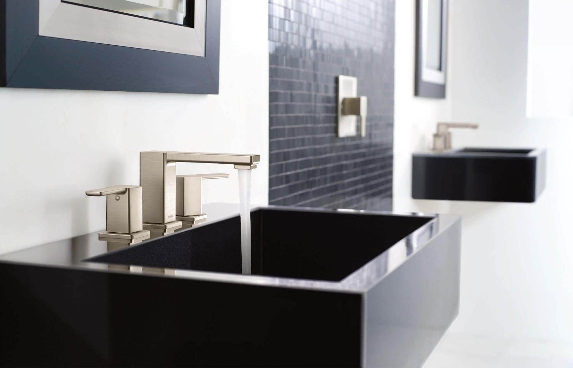 Chrome two-handle widespread bathroom faucet with angular spout mounted on black countertop sink.