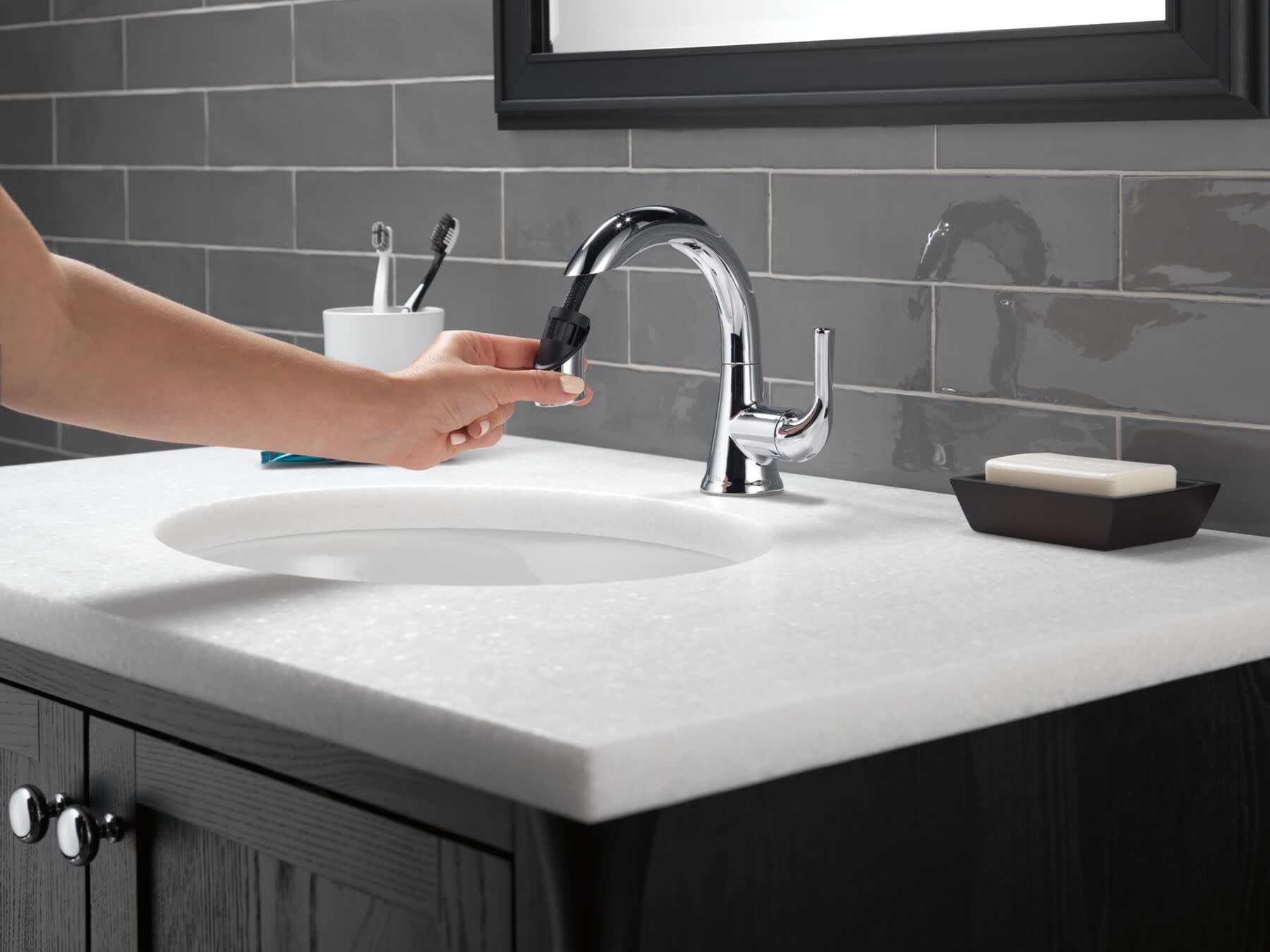 Polished chrome single-handle pull-down faucet with curved spout installed above white bathroom sink.