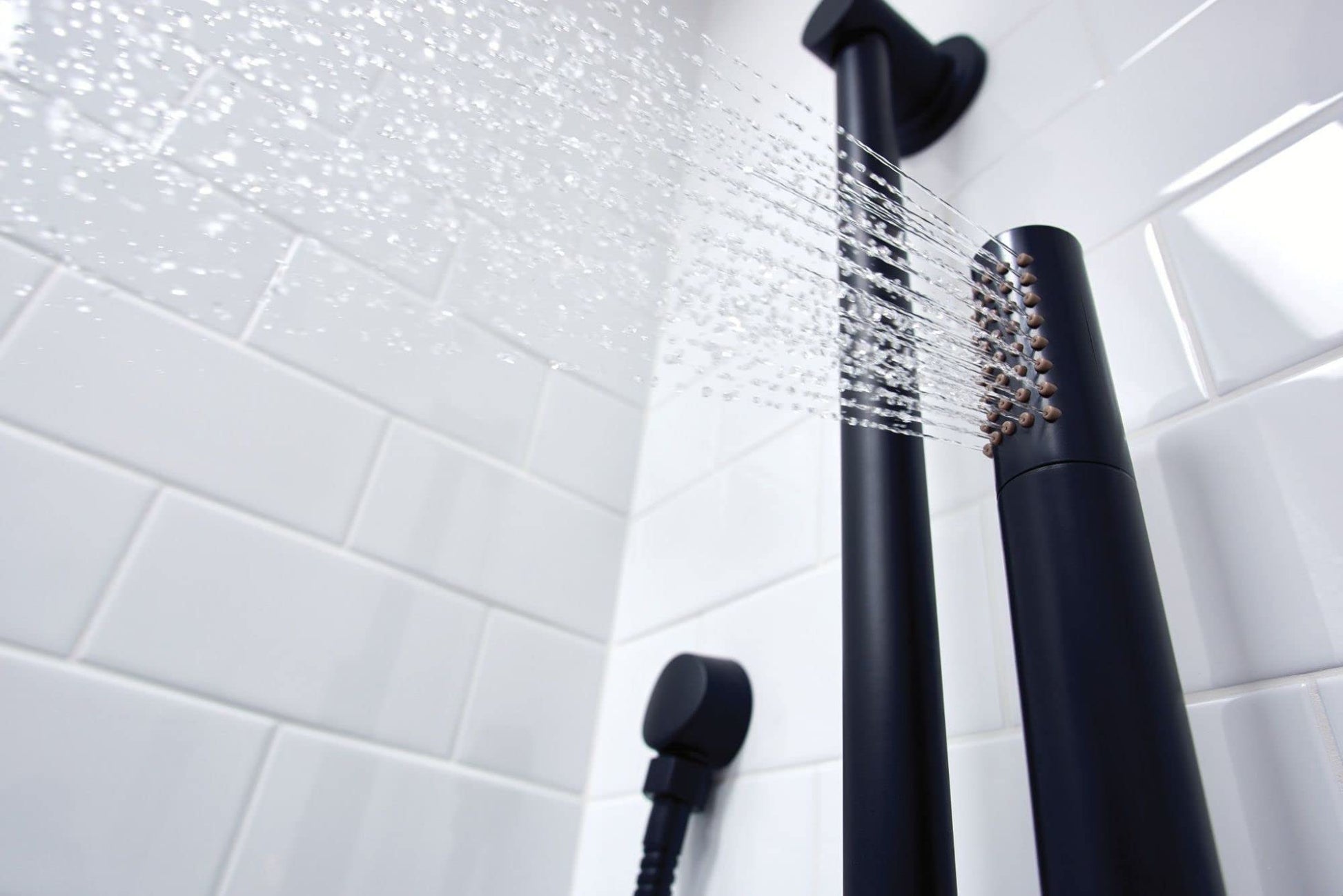 Matte black handheld shower head with adjustable spray pattern mounted on slide bar above white subway tile wall.