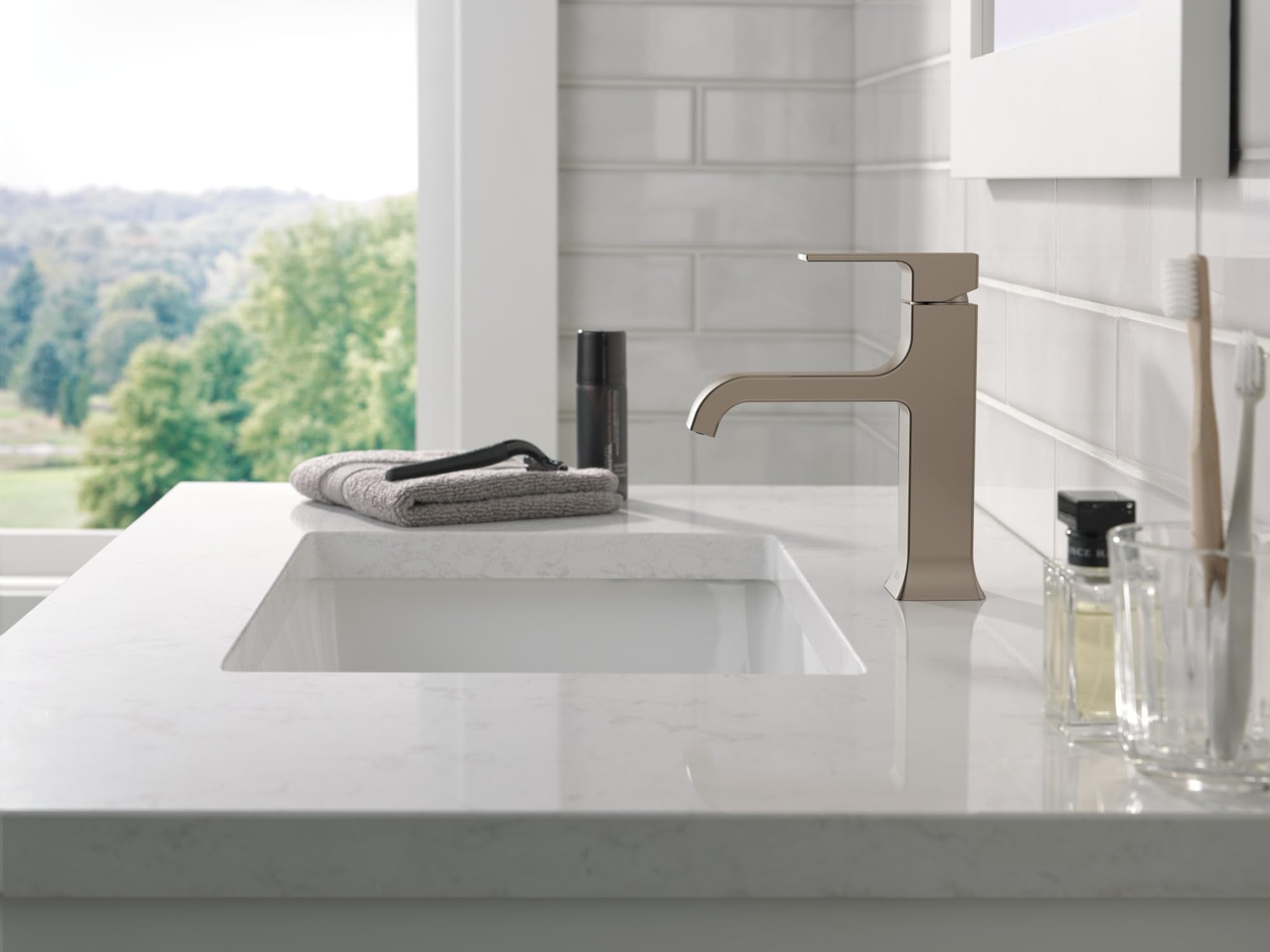 Stainless steel single-handle bathroom faucet with curved spout mounted on white countertop sink.