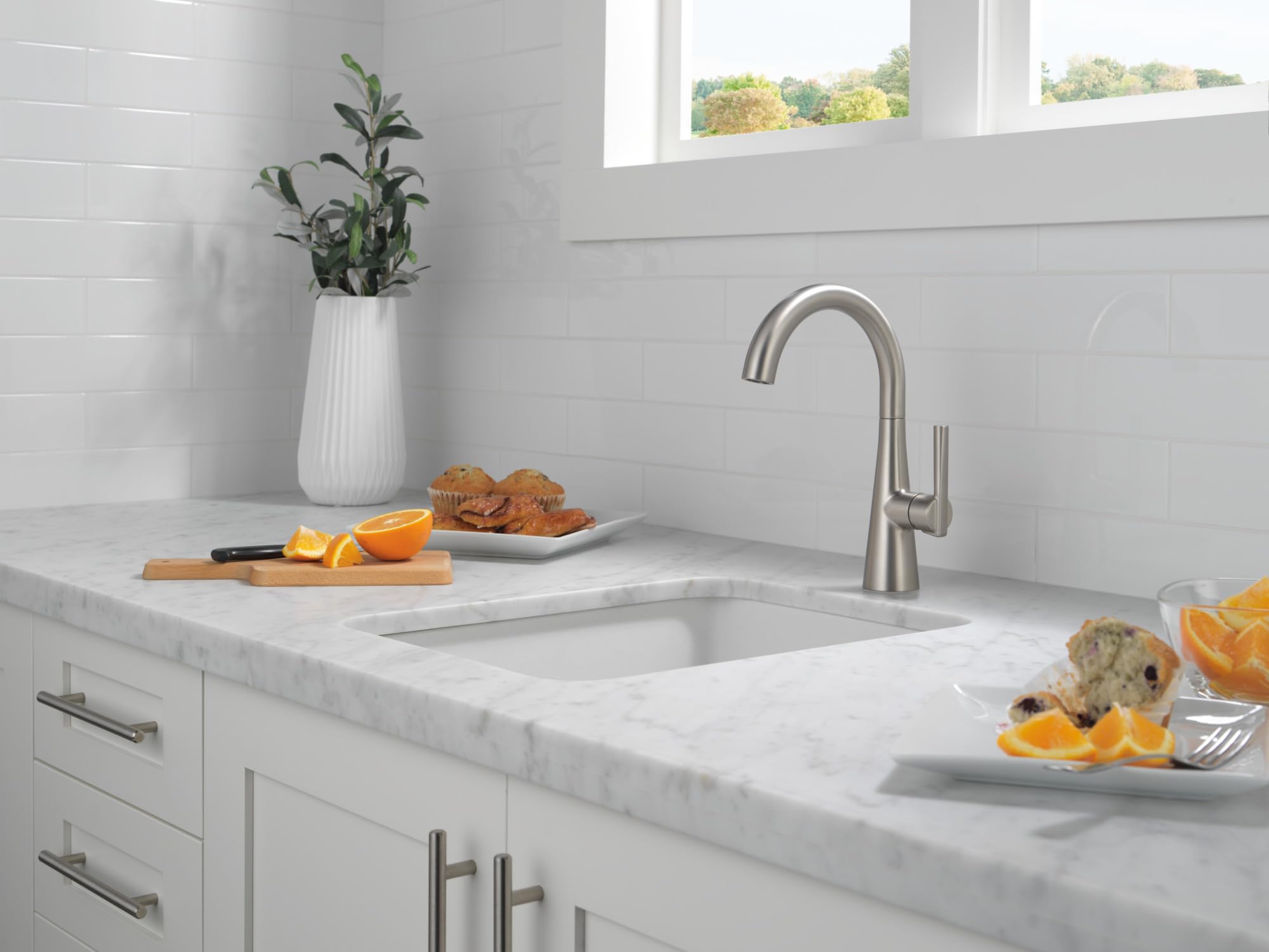 Single-handle bar prep faucet in stainless steel with curved spout, installed above white kitchen sink.