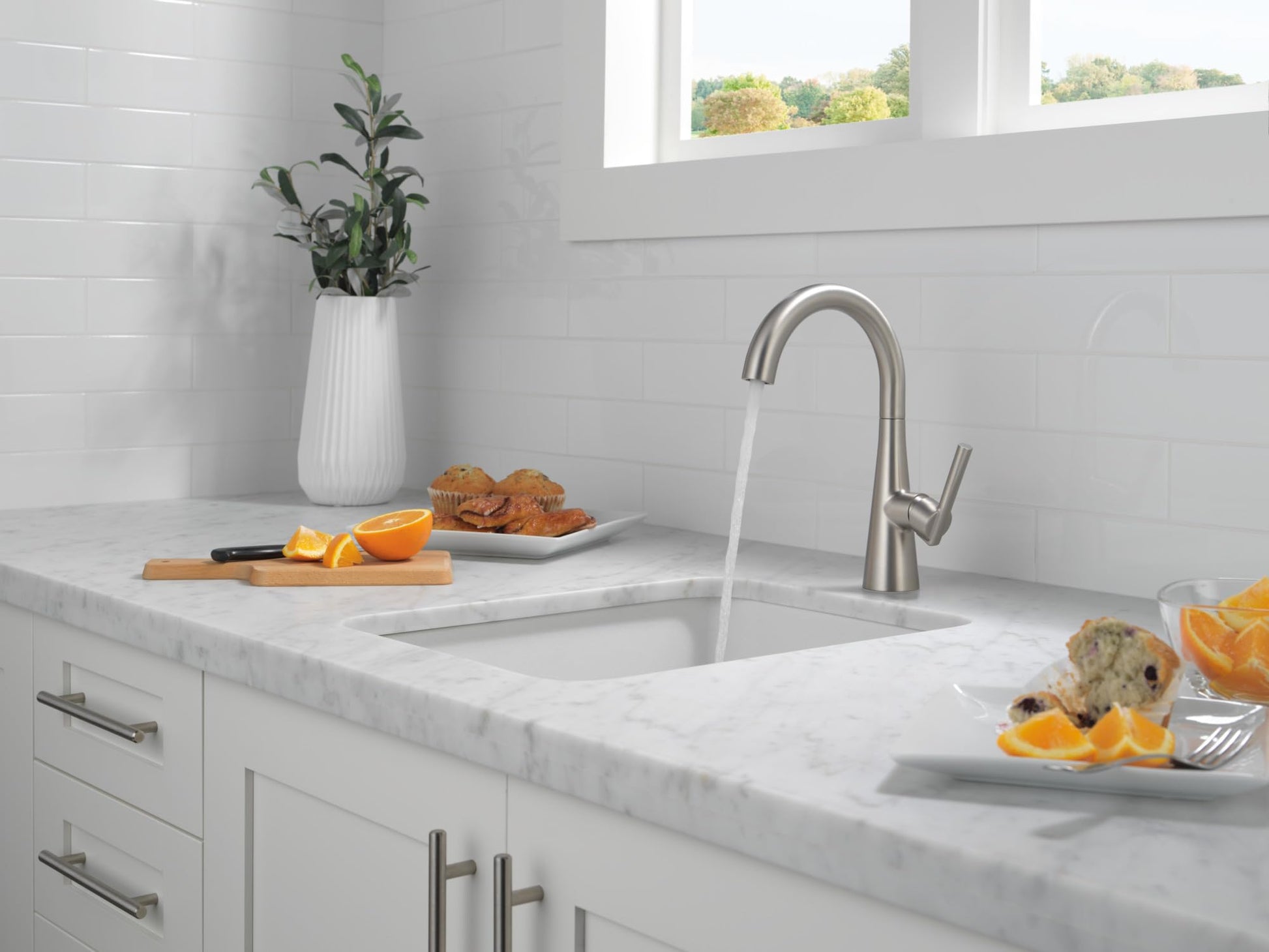 Stainless steel single handle bar prep faucet with curved spout installed above white kitchen sink.