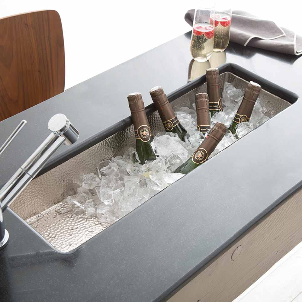 Hammered copper bar sink filled with ice and bottles, featuring a single faucet and textured basin interior.