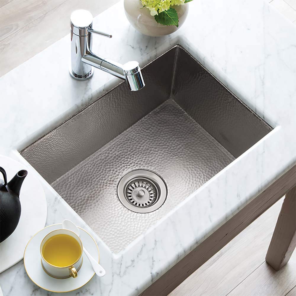 Brushed nickel single-basin kitchen sink with hammered interior, drain strainer, and chrome faucet installed in marble counte