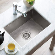 Brushed nickel single-basin kitchen sink with hammered interior, drain strainer, and chrome faucet installed in marble counte