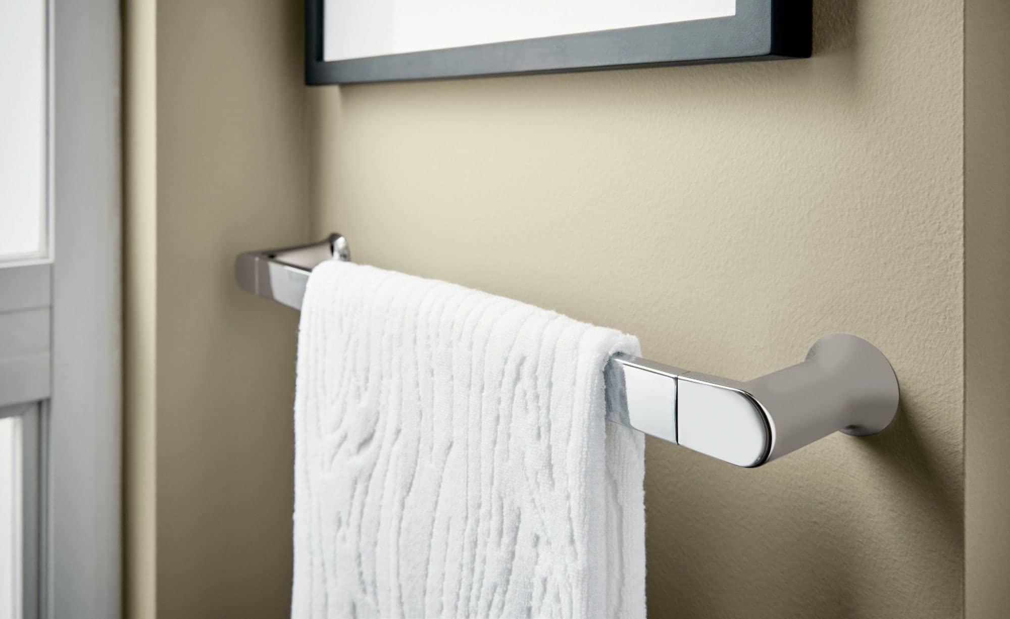 Chrome towel bar mounted on beige wall with white towel draped over it.