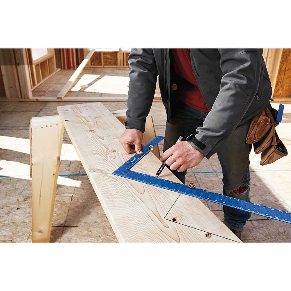 Blue framing square with etched markings being used on lumber in a construction setting.