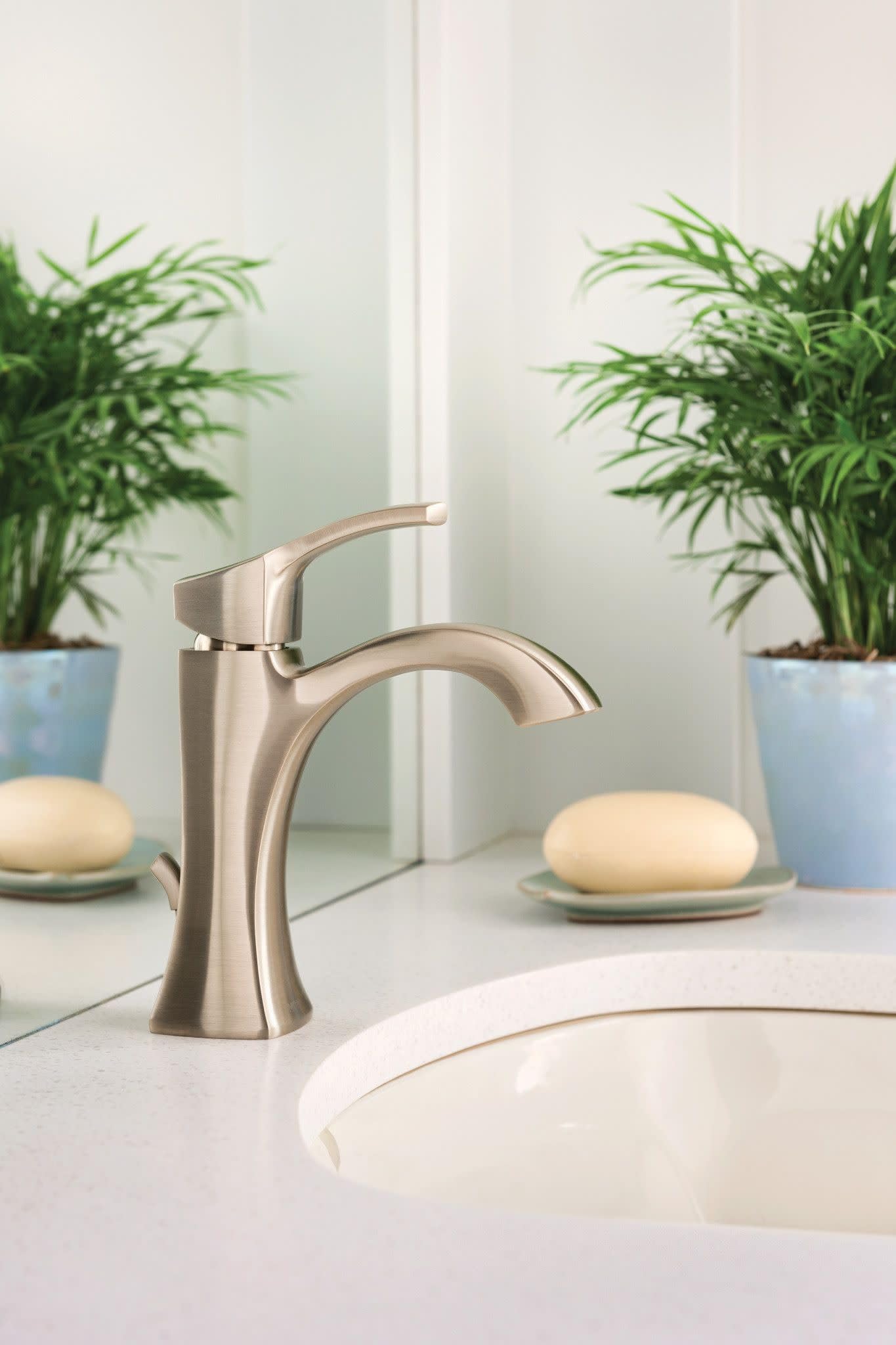 Brushed nickel single-handle bathroom faucet with high arc spout mounted on white sink countertop.