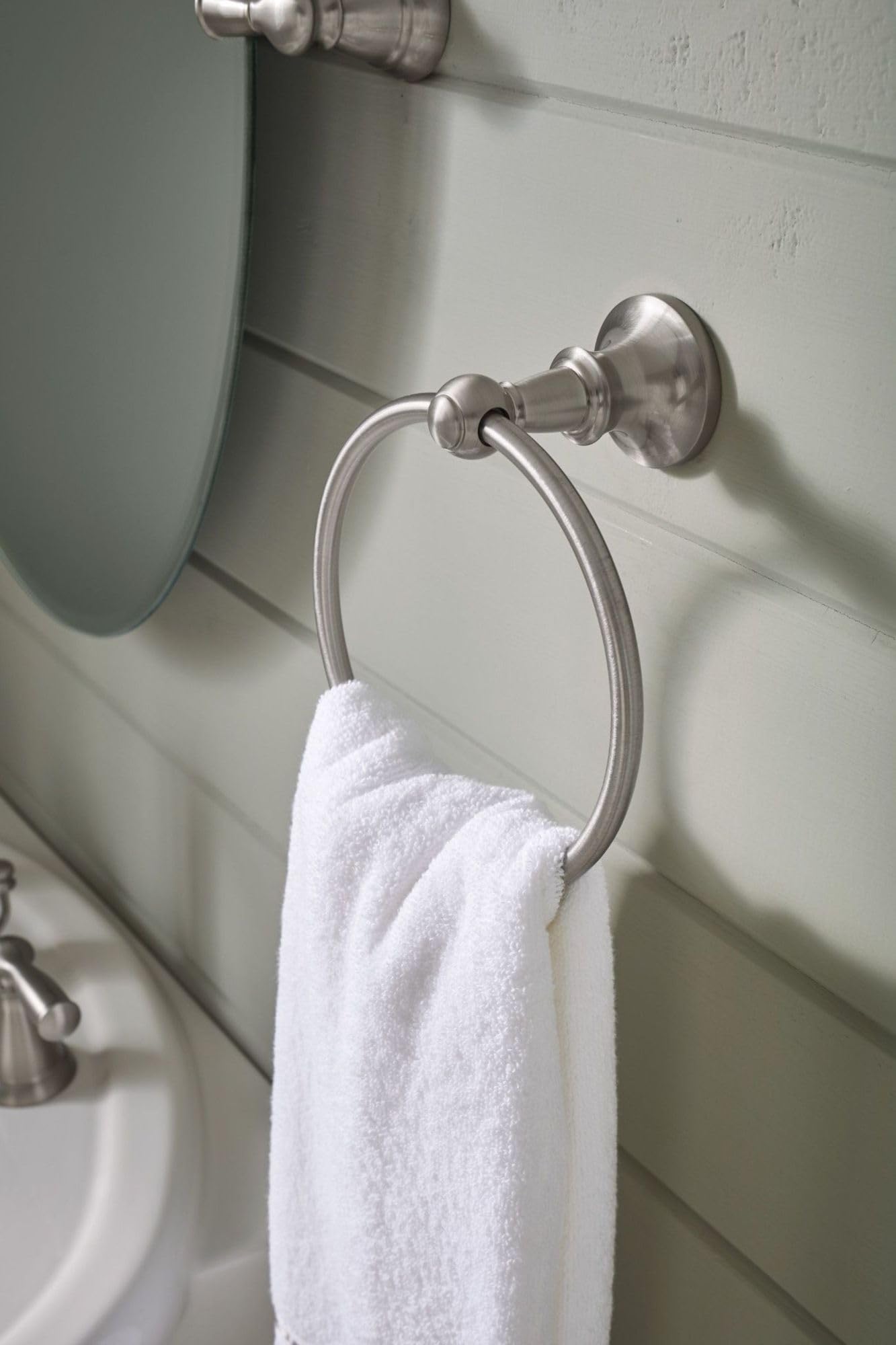 Brushed nickel wall-mounted towel ring with circular design holding a white towel, installed on tiled bathroom wall.