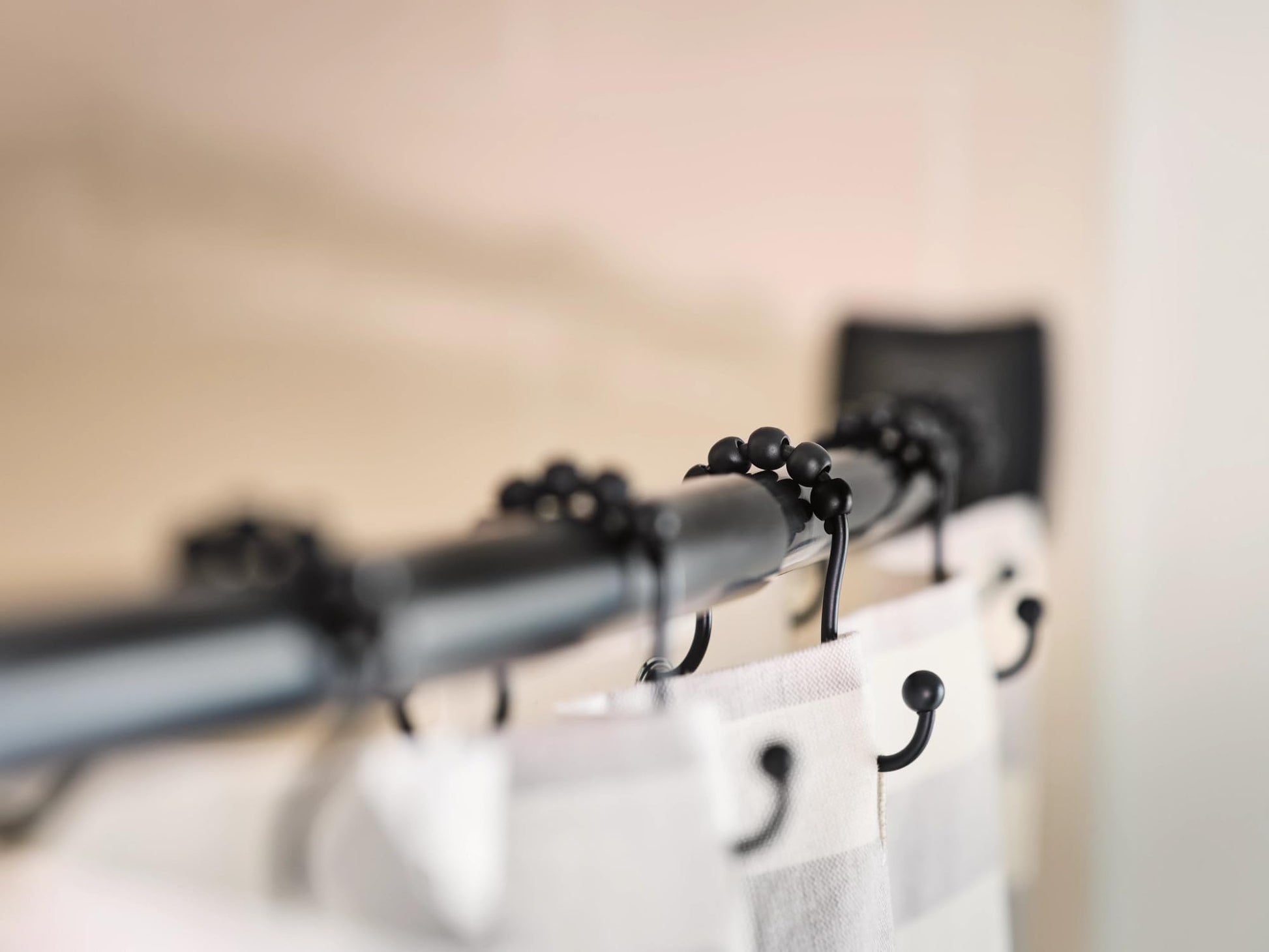 Matte black curved shower rod with multiple hook rings holding white curtain panels.