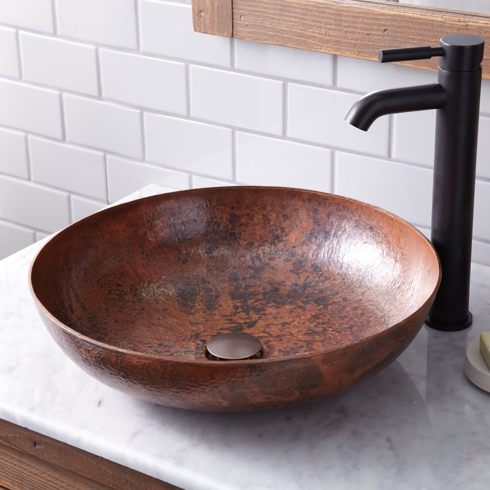 Hammered copper vessel sink with textured brown finish, round bowl shape, paired with black tall faucet on marble countertop.