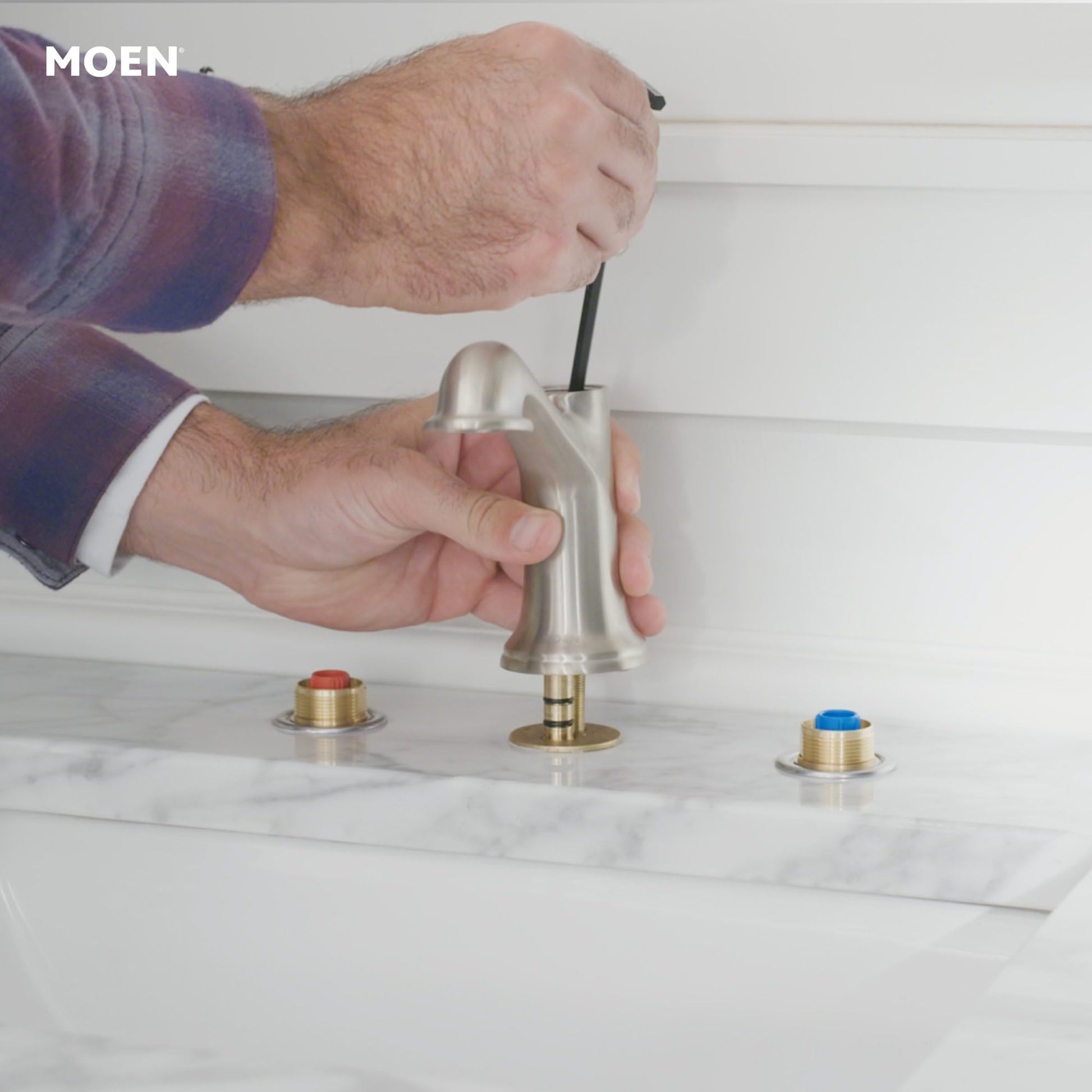 Moen rough-in valve with brass trim rings and blue handle cap being installed on marble countertop.