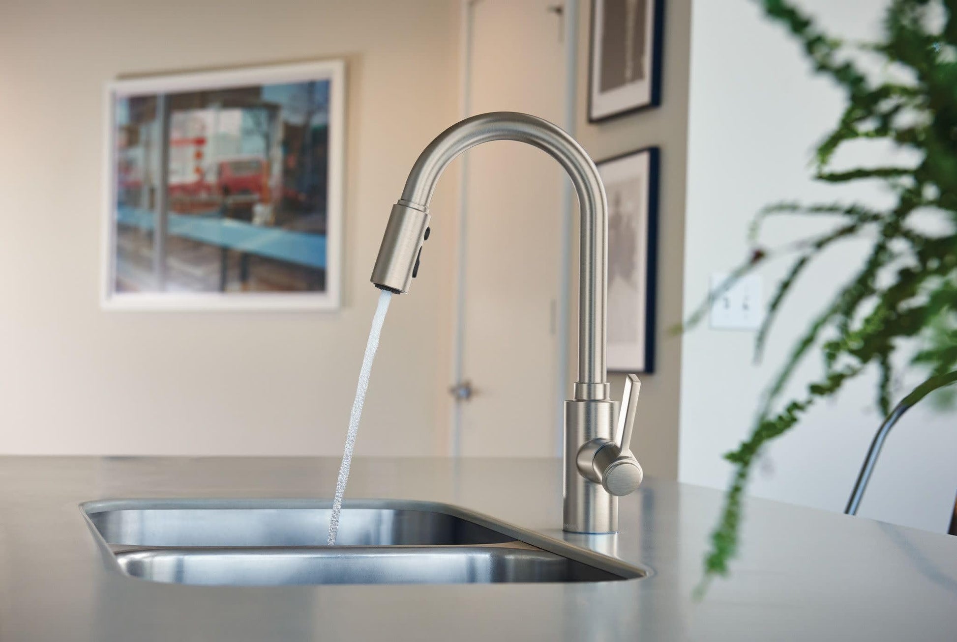 Stainless steel kitchen faucet with arched spout and pulldown sprayer head dispensing water into sink.