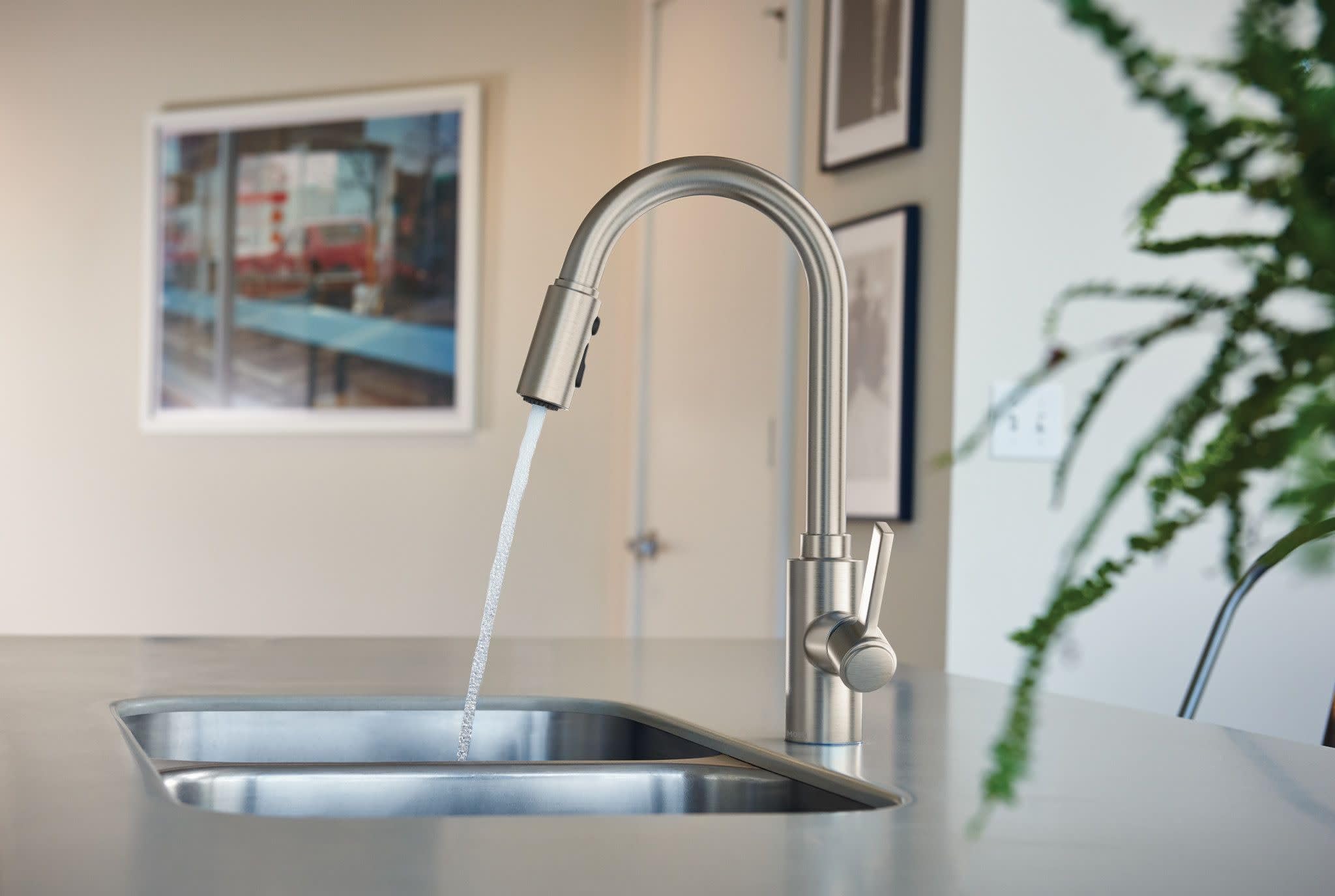 Stainless steel kitchen faucet with arched spout and pulldown sprayer head dispensing water into sink.