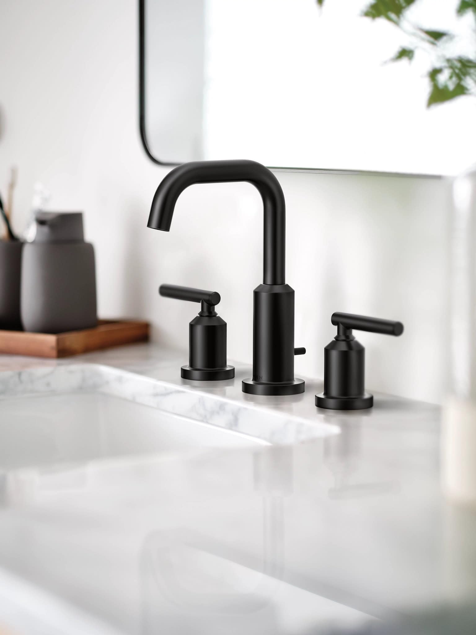 Matte black three-piece widespread bathroom faucet with curved spout and lever handles on white marble counter.