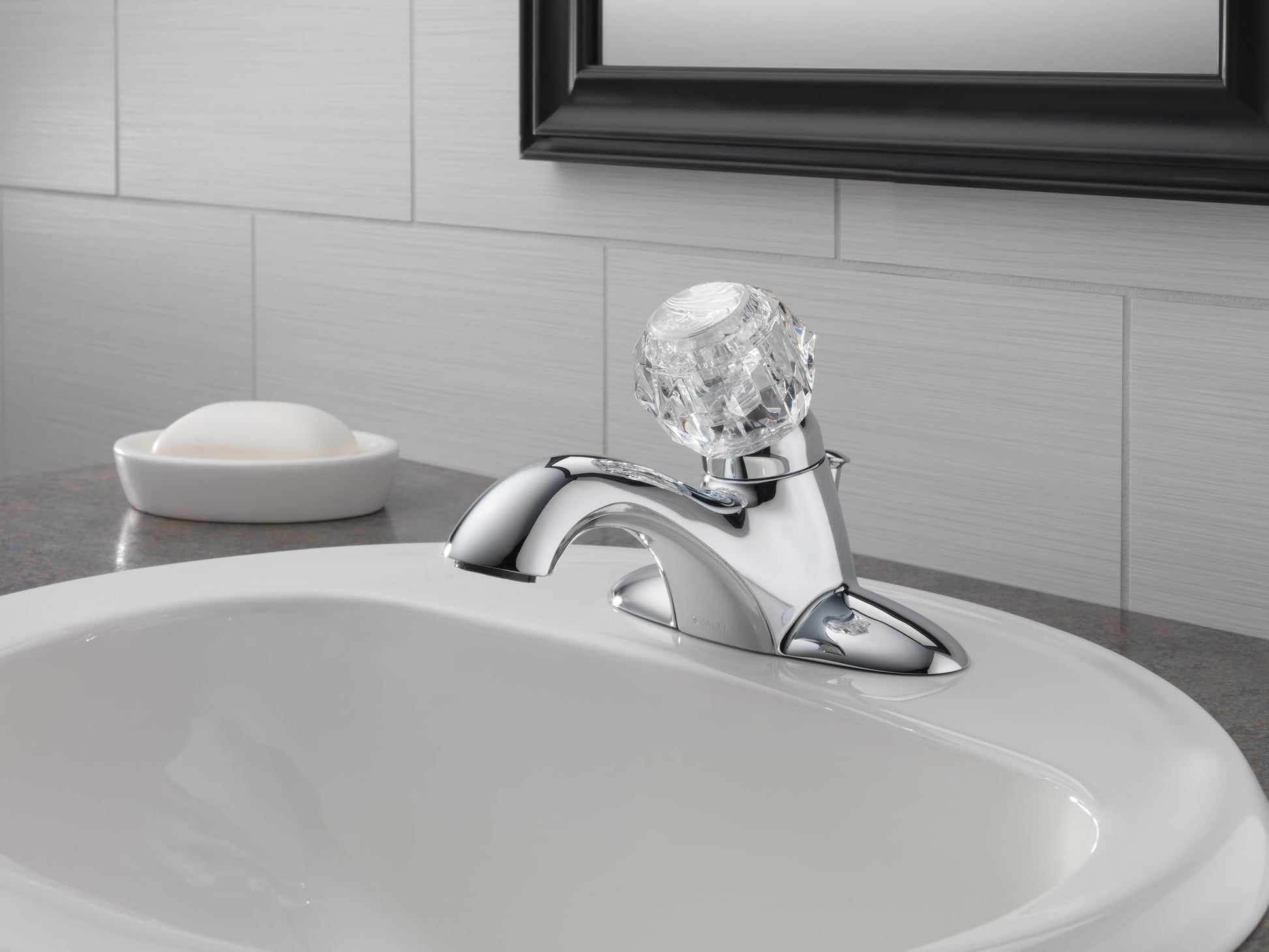 Chrome single-handle bathroom faucet with curved spout and crystal handle installed on white sink.
