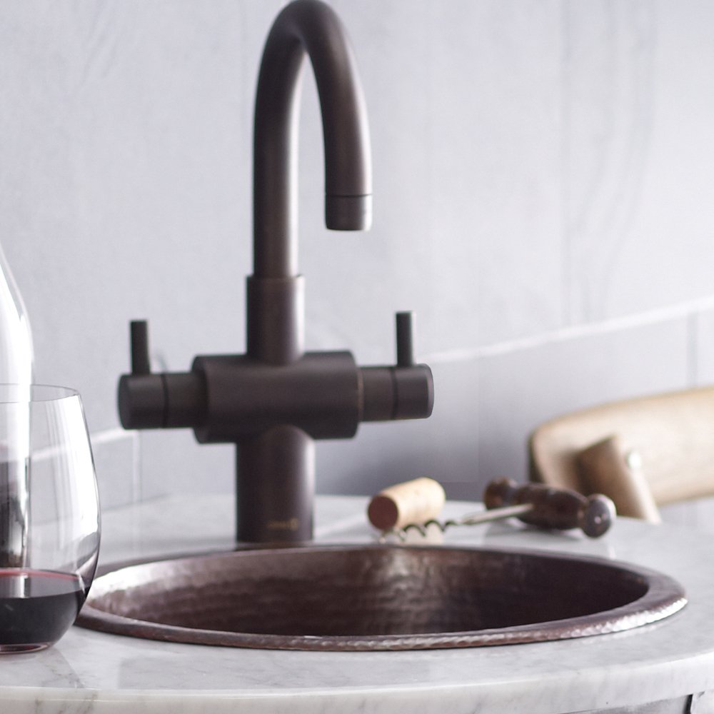 Hammered copper bar sink with antique finish and matte black gooseneck faucet with dual handles.