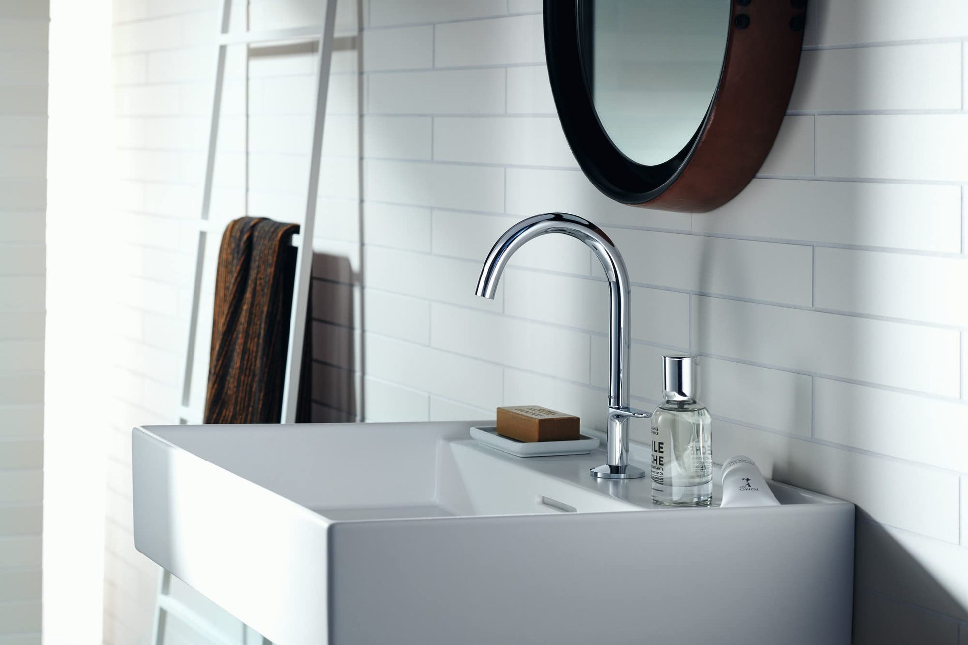 Chrome single-hole bathroom faucet with curved spout mounted above white rectangular sink.