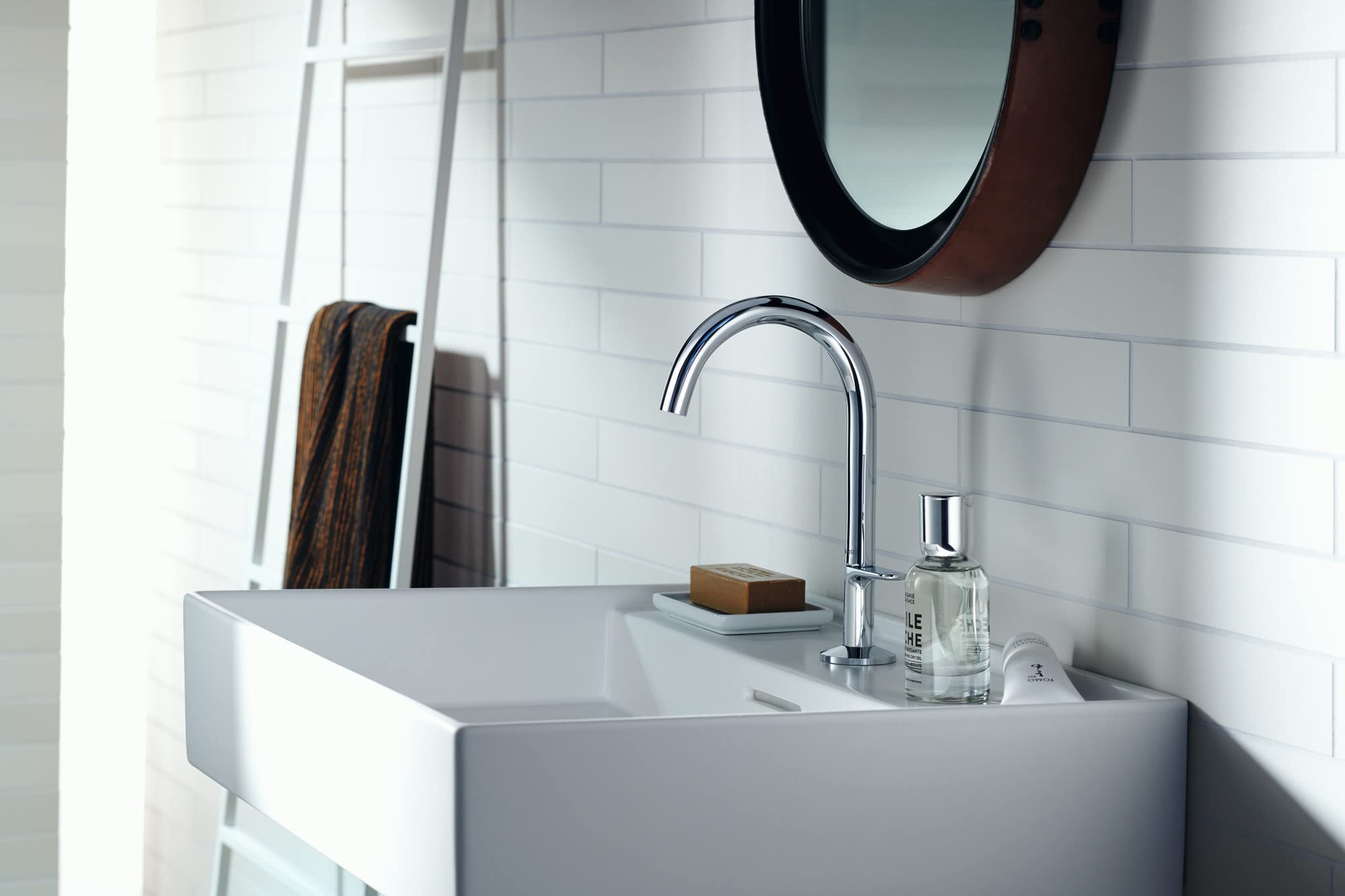 Chrome single-hole bathroom faucet with curved spout mounted above white rectangular sink.