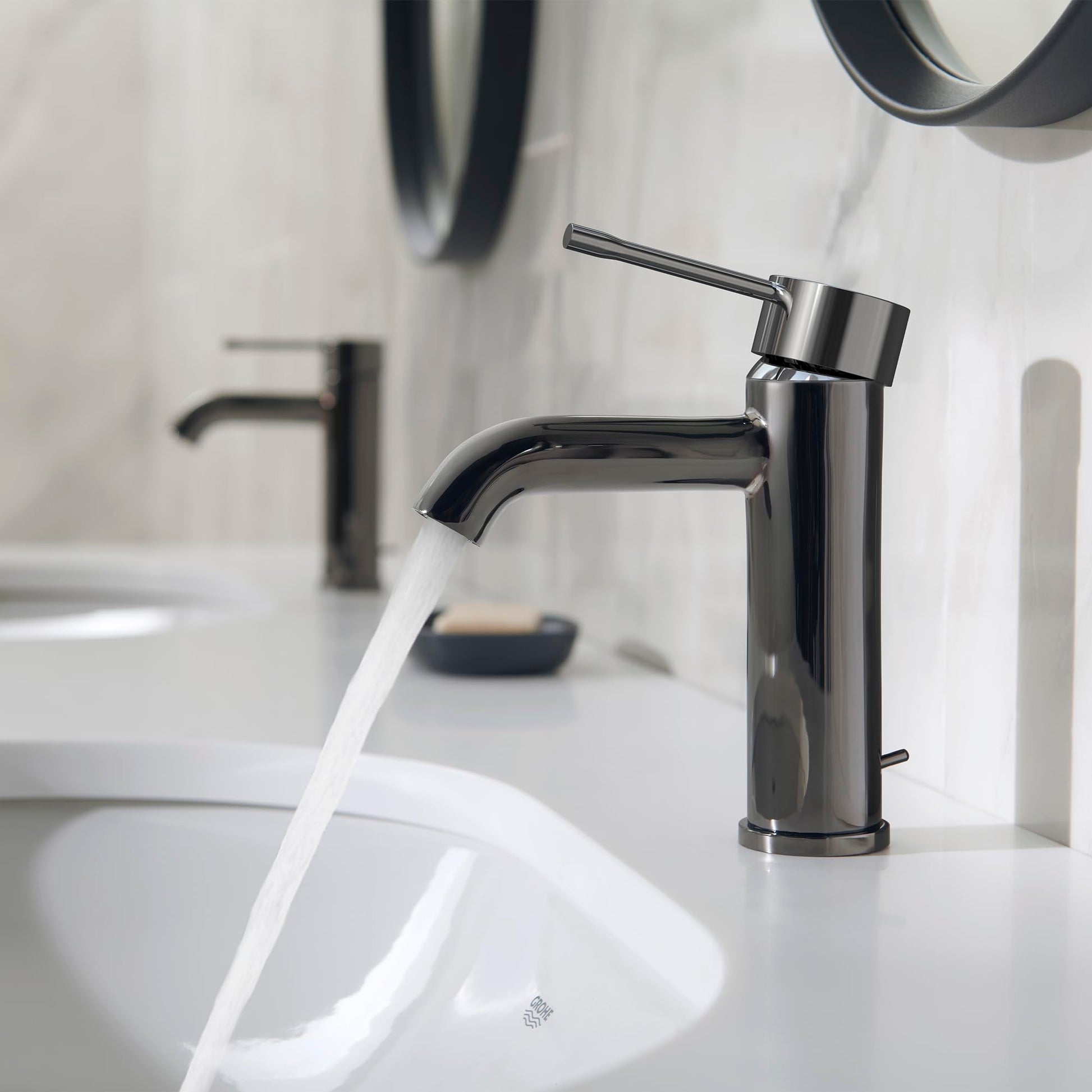 Dark graphite single-handle bathroom faucet with curved spout dispensing water into white sink.
