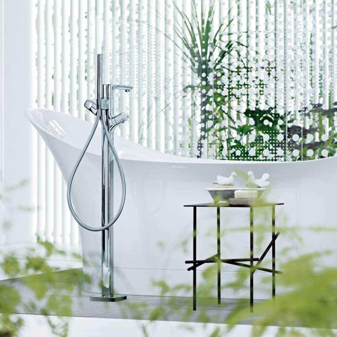 White freestanding bathtub with curved sides and chrome floor-mounted faucet with handheld showerhead.