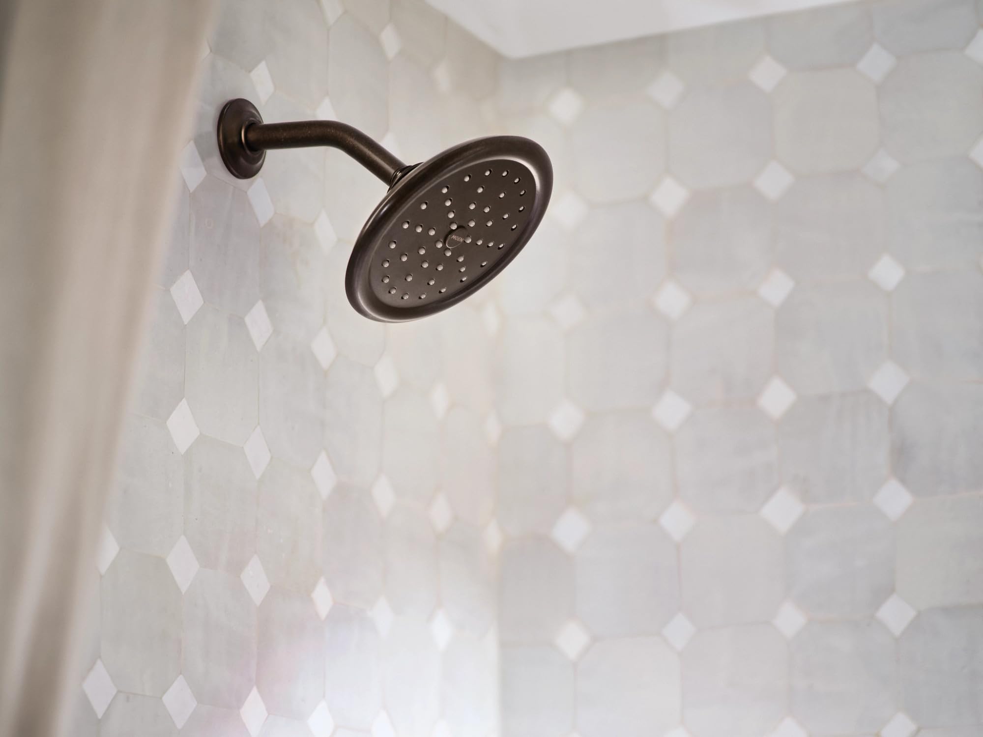 Oil rubbed bronze showerhead with curved arm mounted on tiled shower wall.
