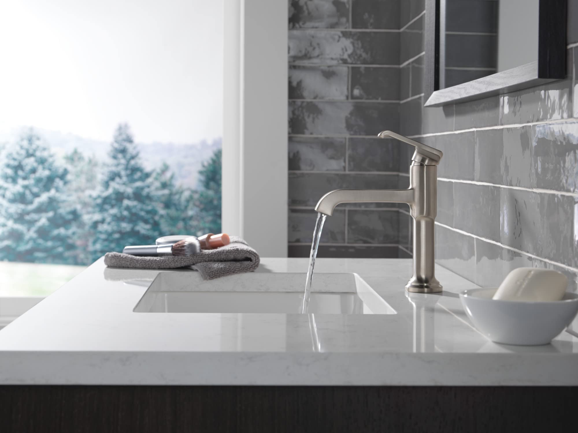 Stainless steel single-handle bathroom faucet with curved spout installed above white sink countertop.
