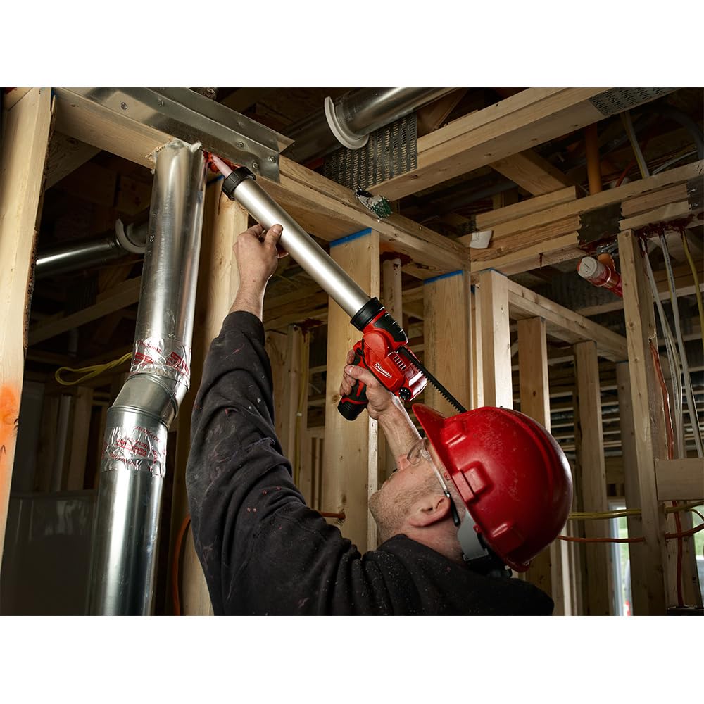 Red and silver cordless caulk gun being used to apply sealant to metal framing in construction setting.