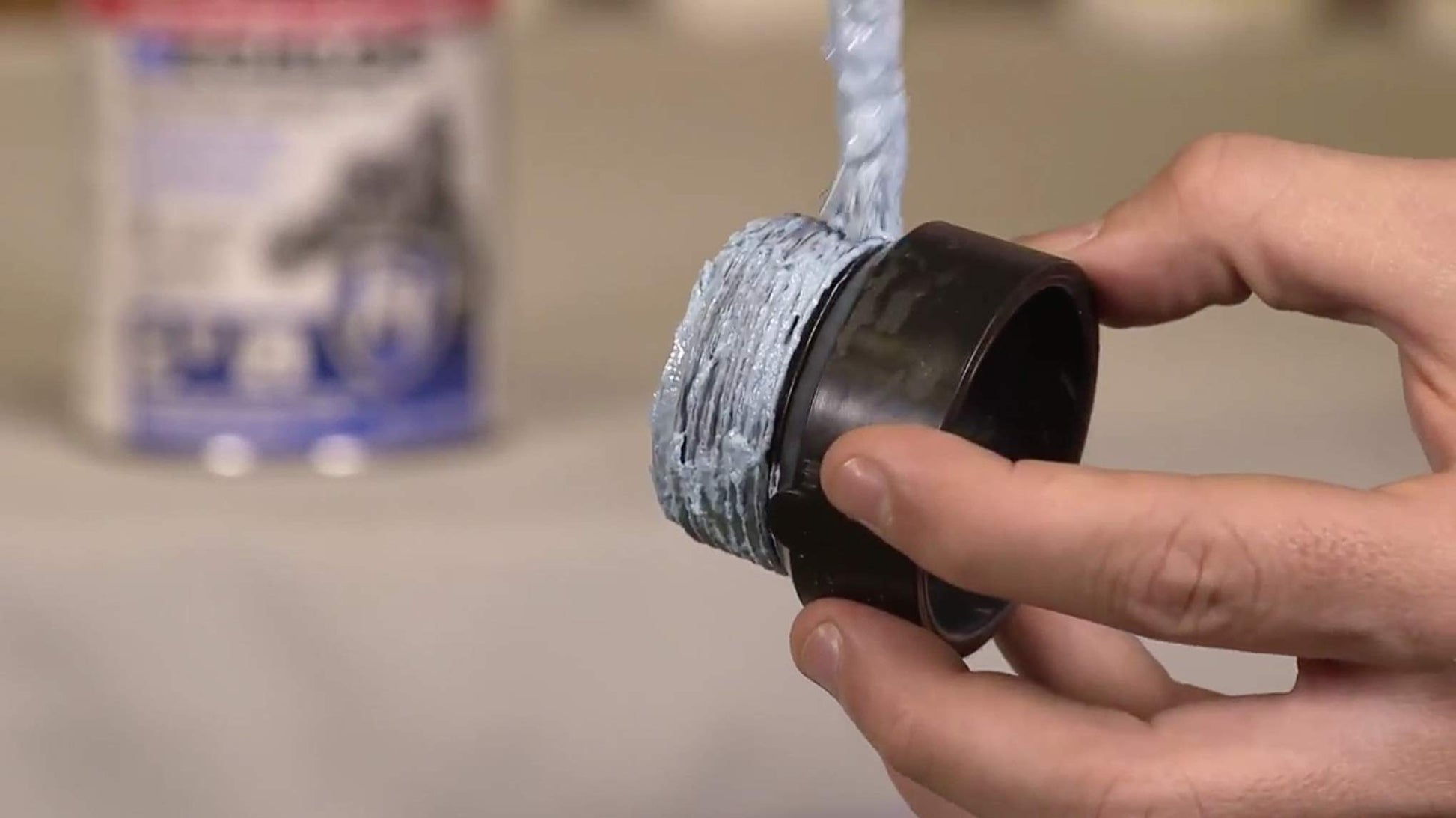 Hand holding open container of blue thread sealant compound with brush applicator extending upward.