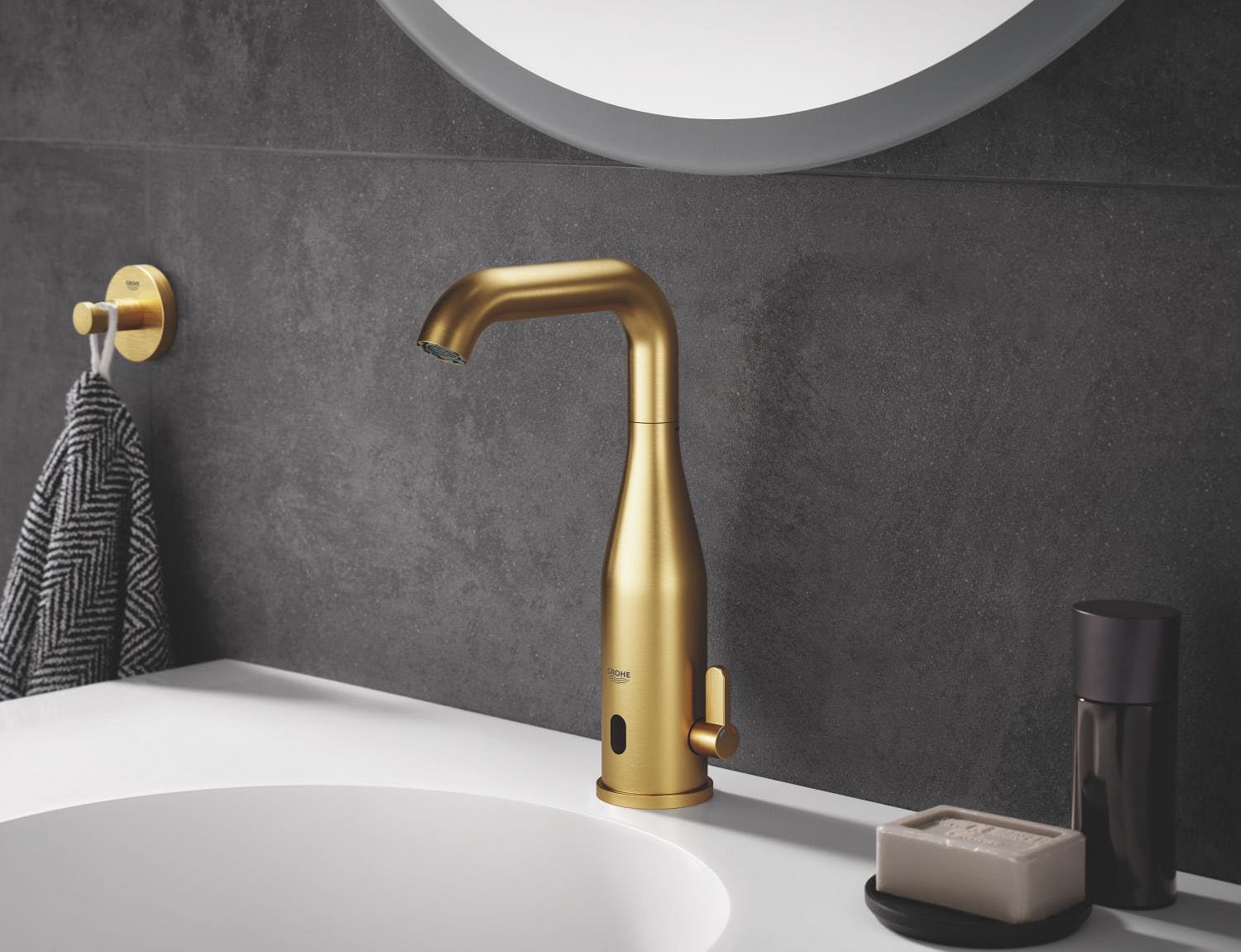 Brushed gold robe hook mounted on dark tile wall next to bathroom sink.