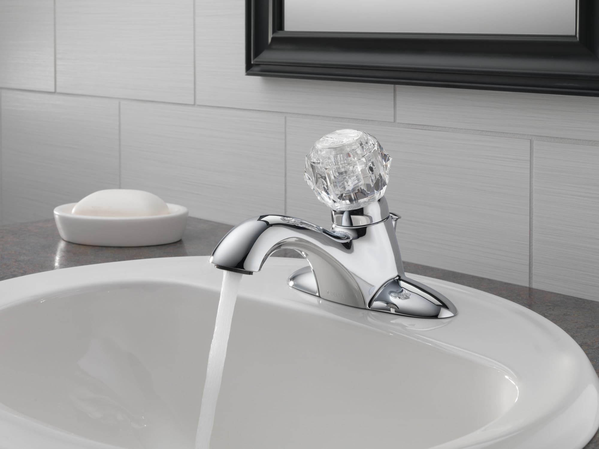 Chrome single-handle bathroom faucet with curved spout and crystal knob installed on white sink.