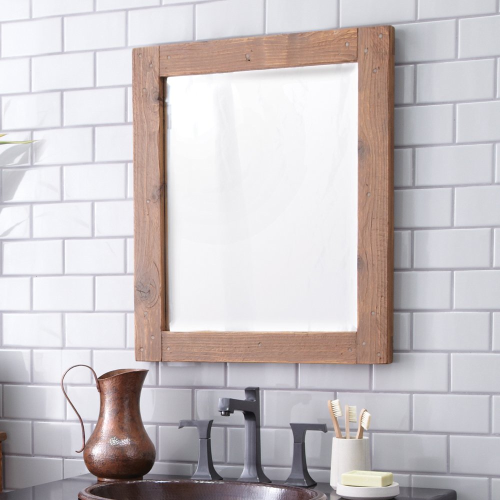 Rectangular mirror with chestnut wood frame mounted on white subway tile wall above bathroom vanity.