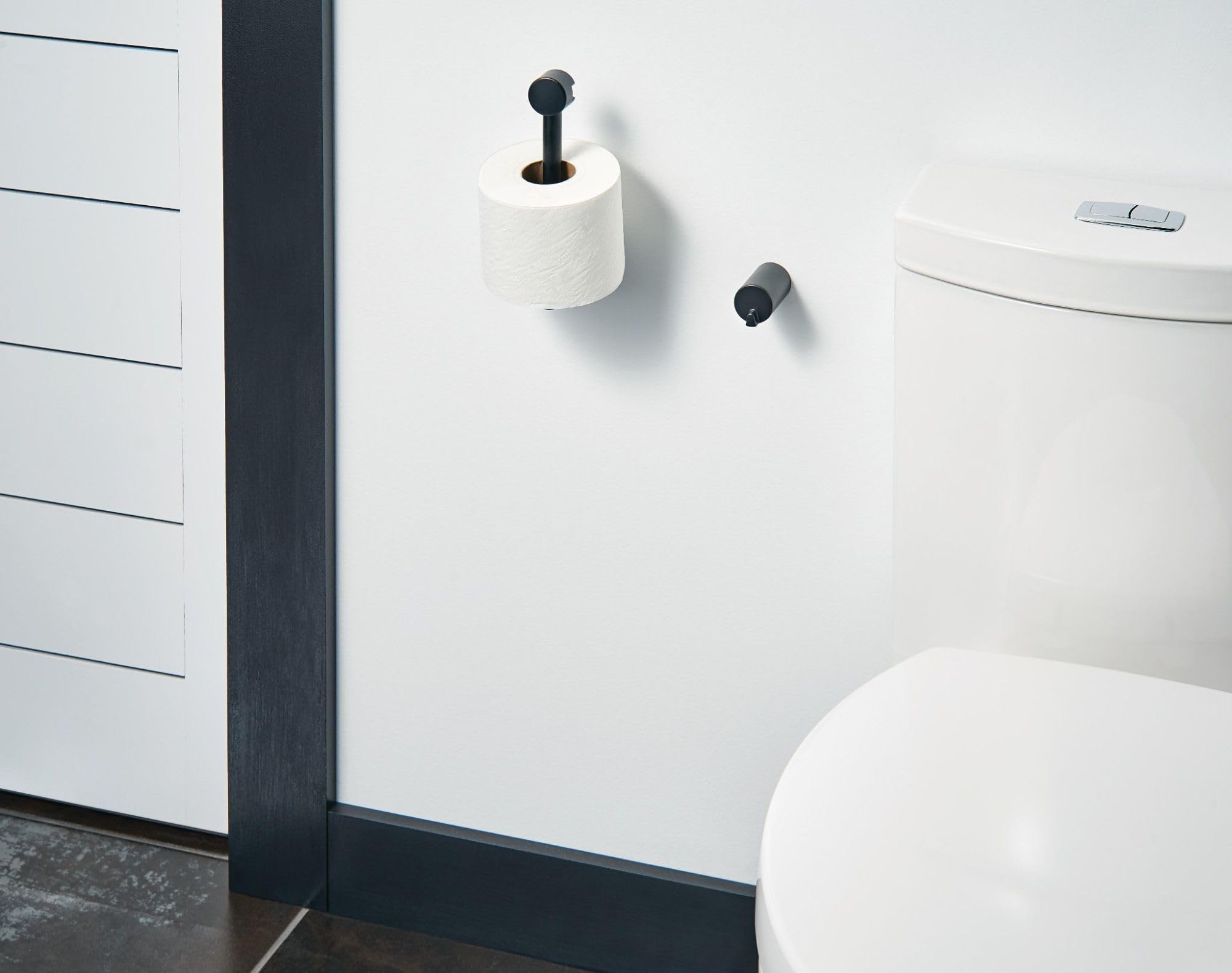 Black pivoting toilet paper holder mounted on white bathroom wall with roll installed.