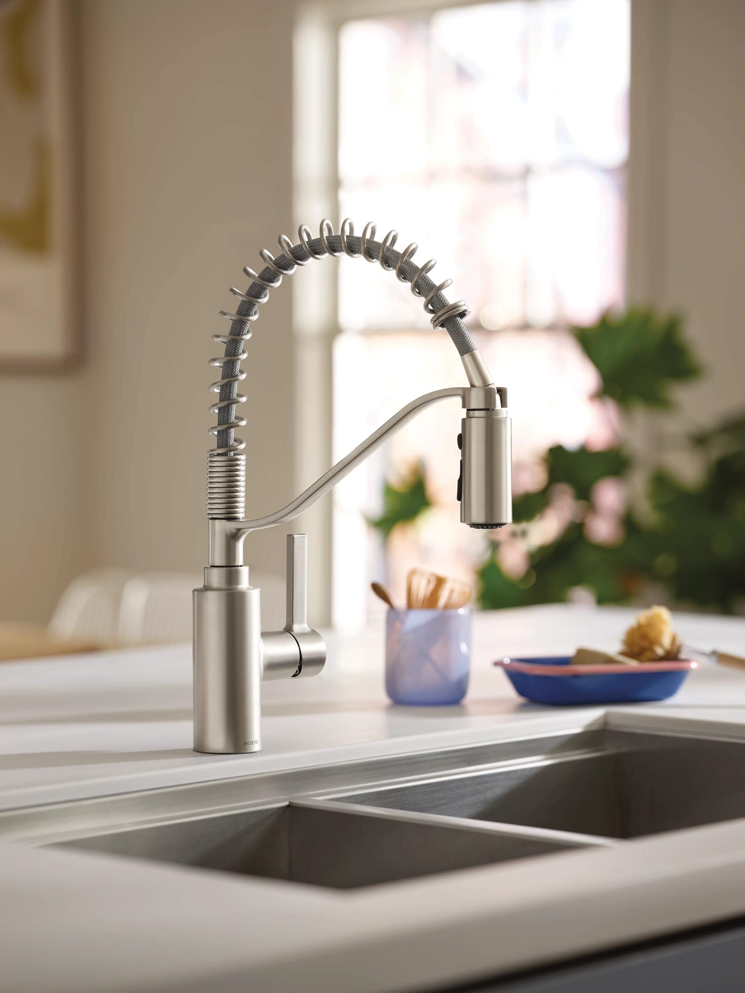 Stainless steel spring kitchen faucet with single handle and pre-rinse spray mounted above double sink.