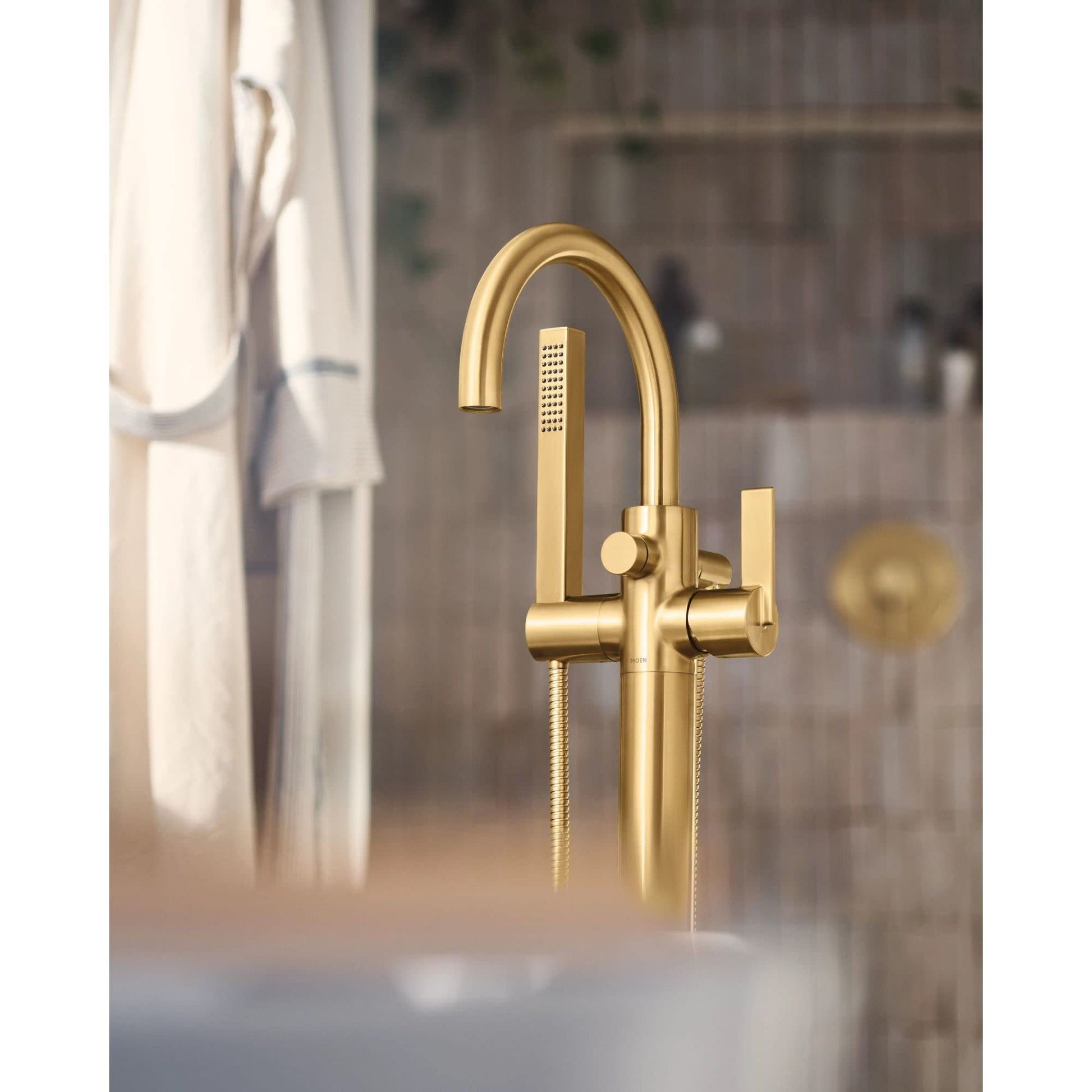 Gold-finish freestanding tub filler with curved spout, single handle, and handheld showerhead attached by hose.