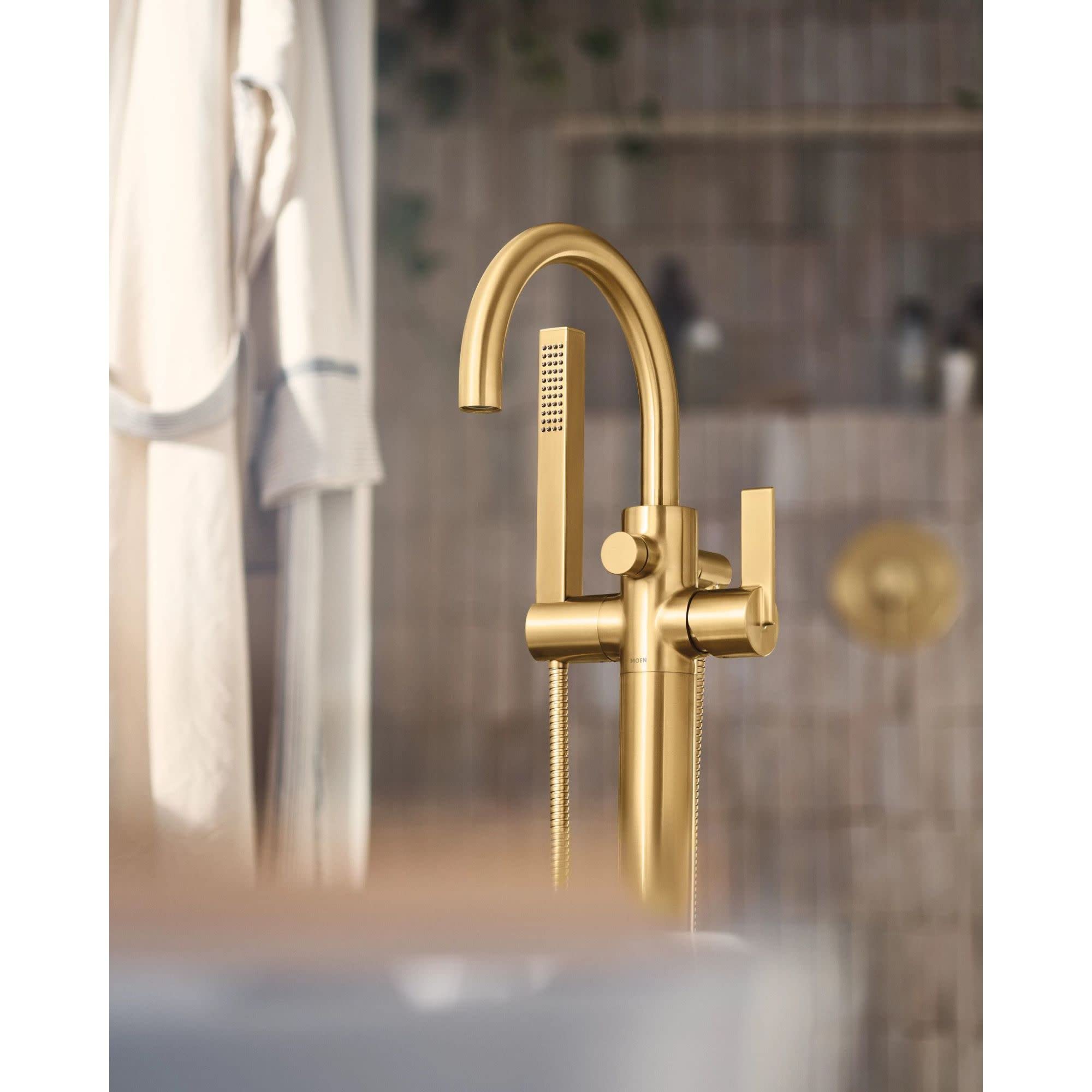 Gold-finish freestanding tub filler with curved spout, single handle, and handheld showerhead attached by hose.