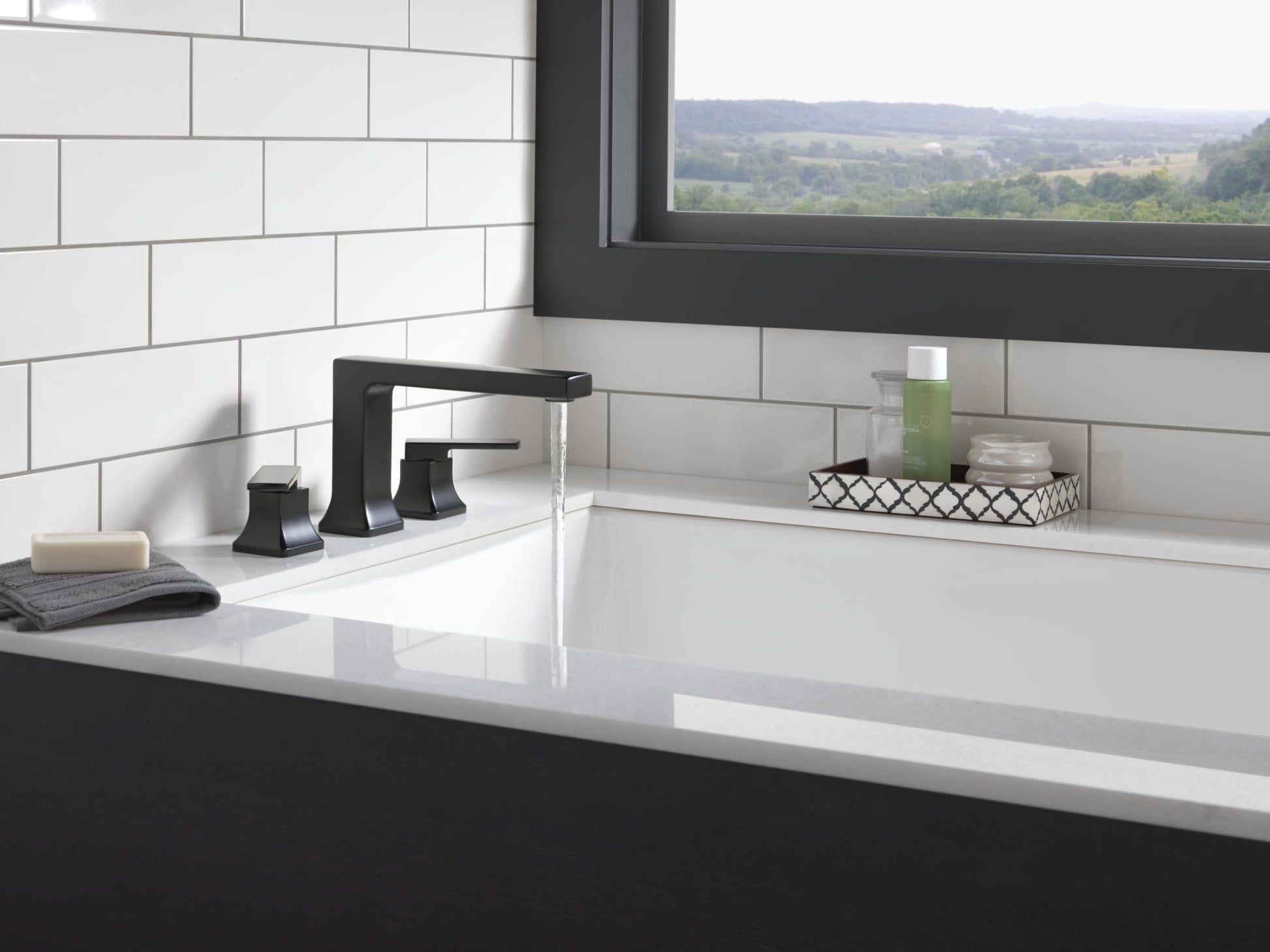 Matte black three-hole Roman tub trim with lever handles and arched spout installed on white countertop.