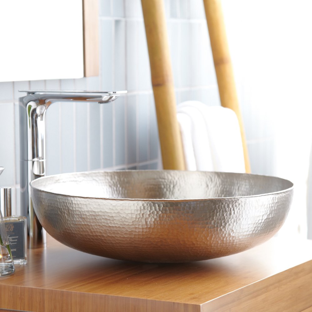Hammered copper vessel sink with wide bowl shape and textured surface on wooden countertop.