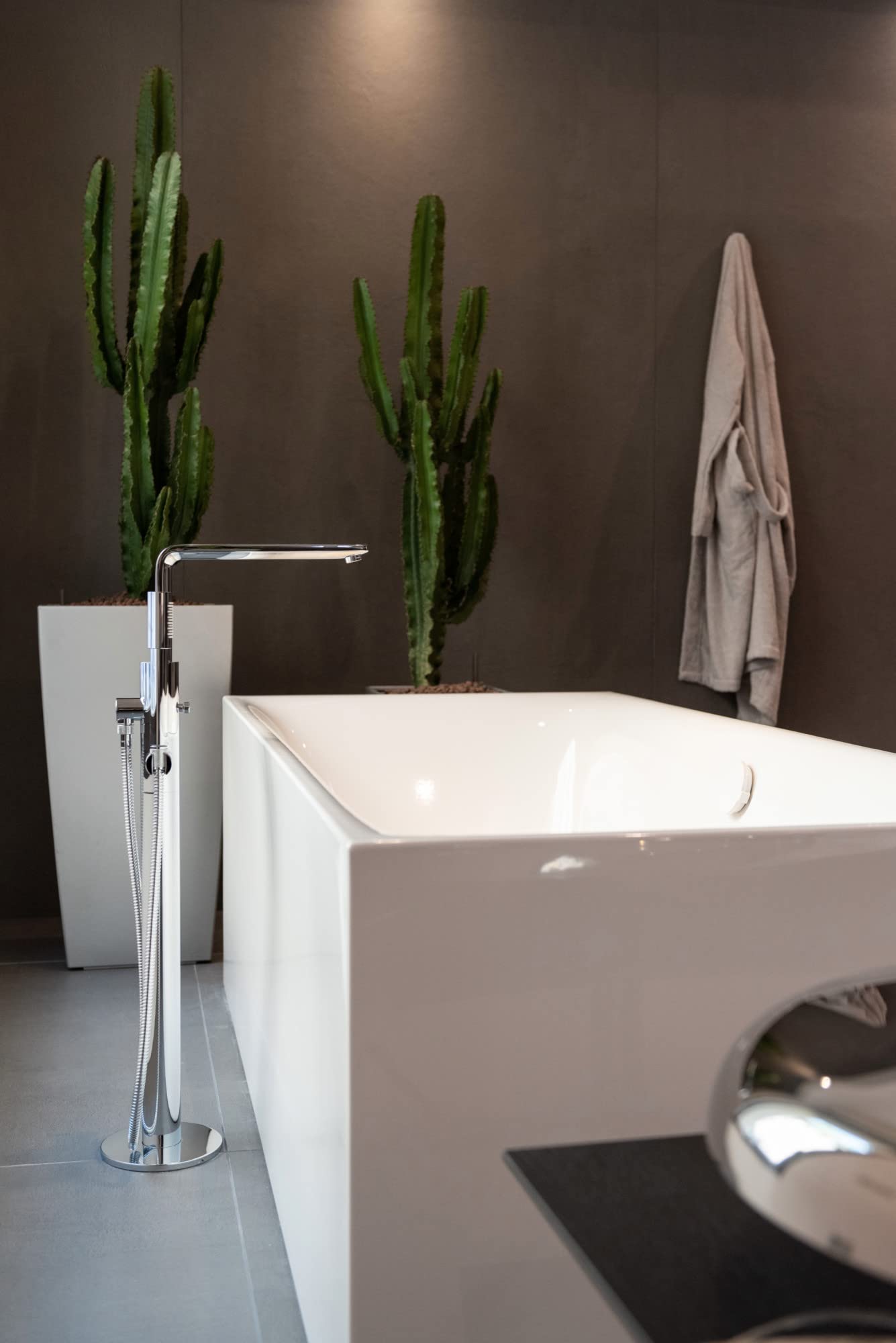 Brushed nickel single-handle freestanding tub faucet with hand shower hose next to white soaking tub.