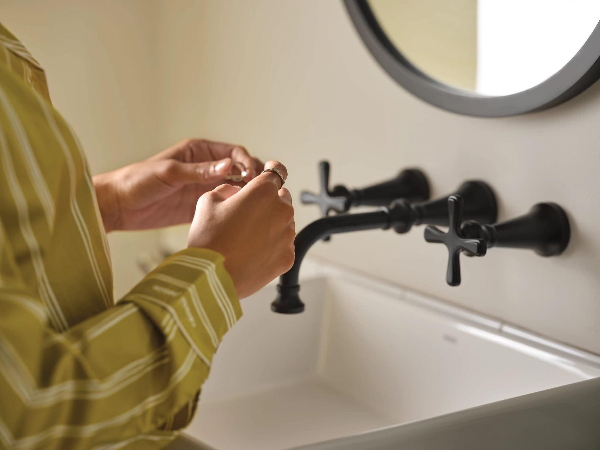 Matte black wall-mounted bathroom faucet with cross handles installed above white sink basin.