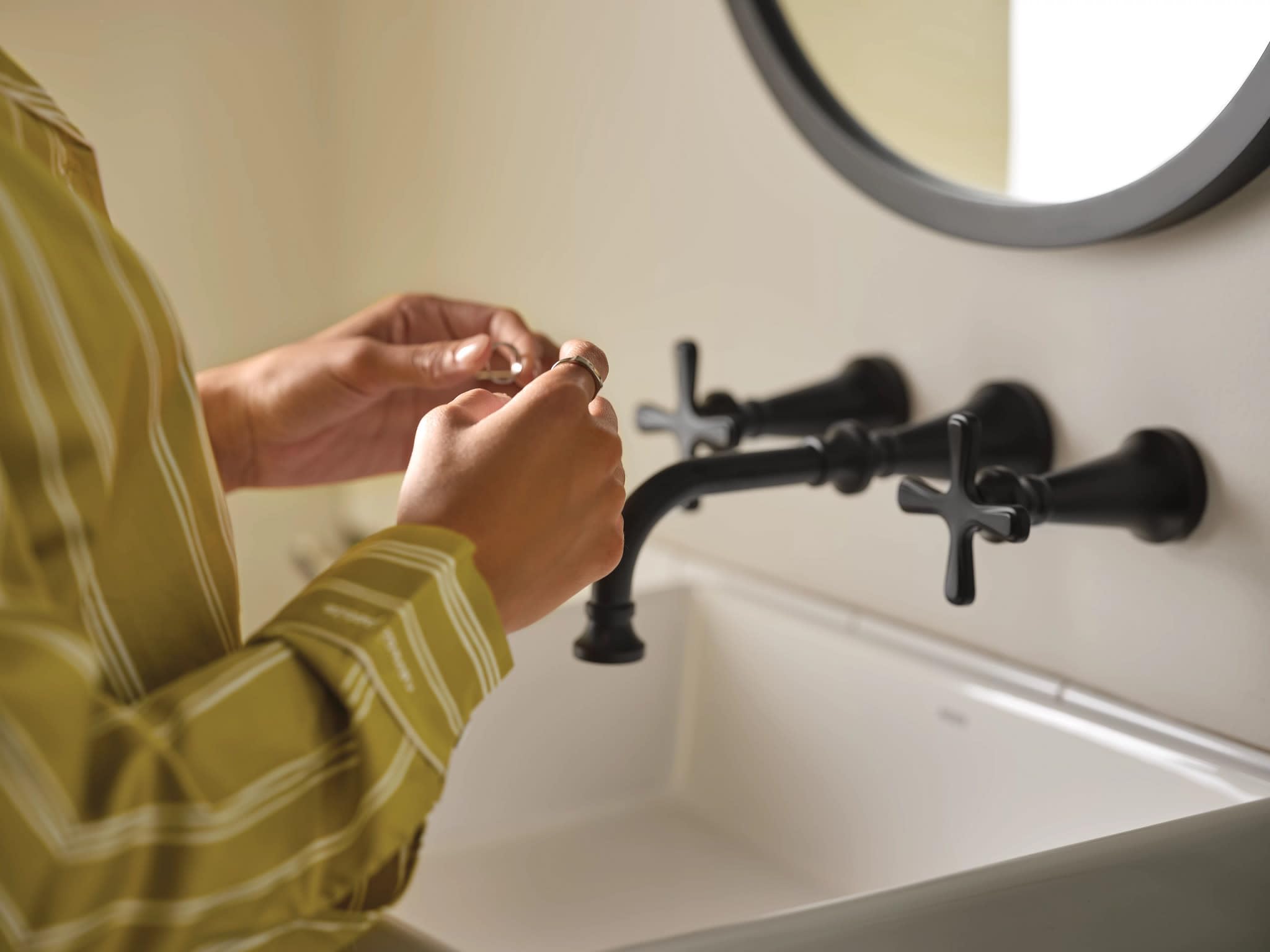 Matte black wall-mounted bathroom faucet with cross handles installed above white sink basin.