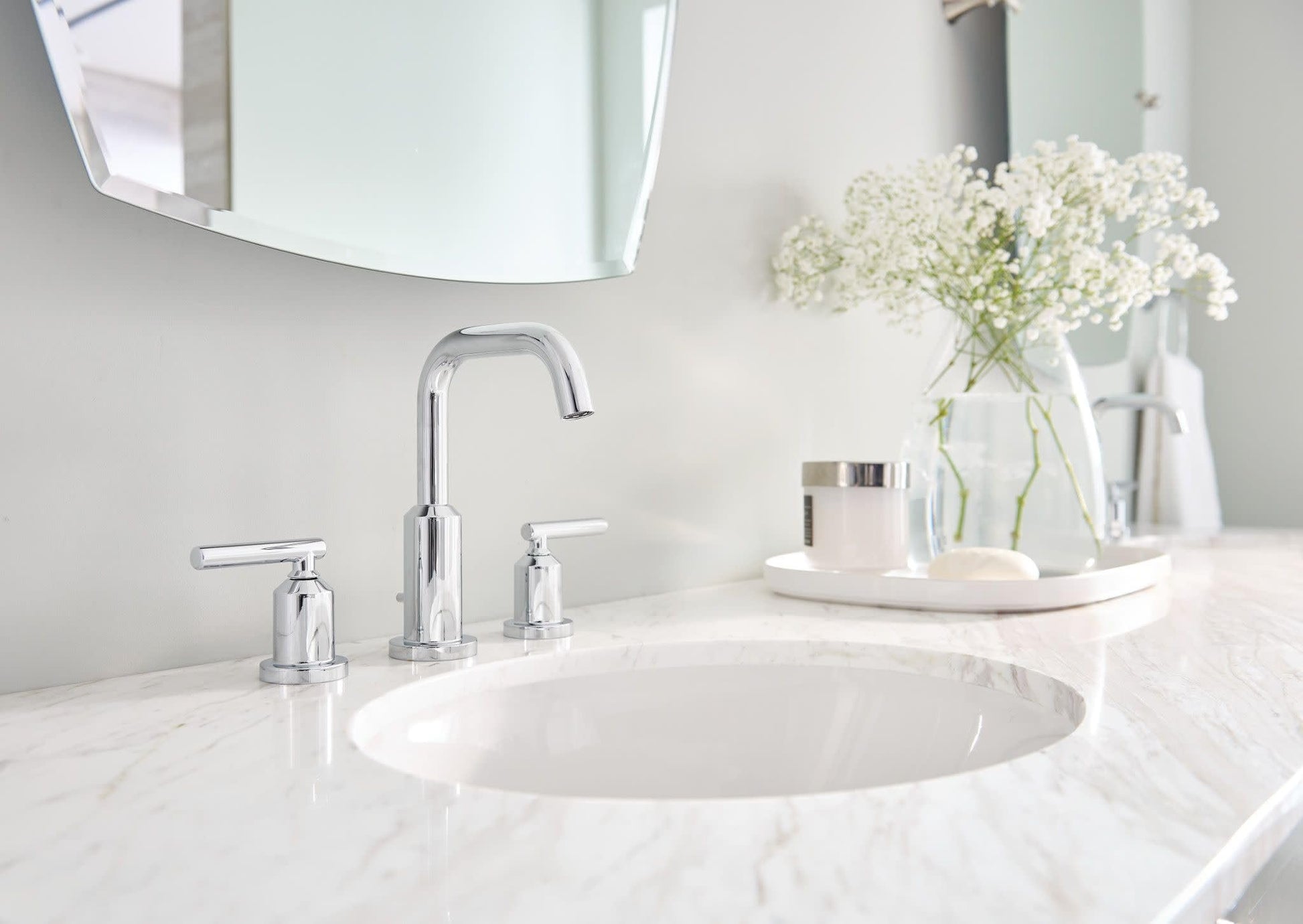 Chrome widespread bathroom sink faucet with high arc spout and two handles installed on marble countertop.
