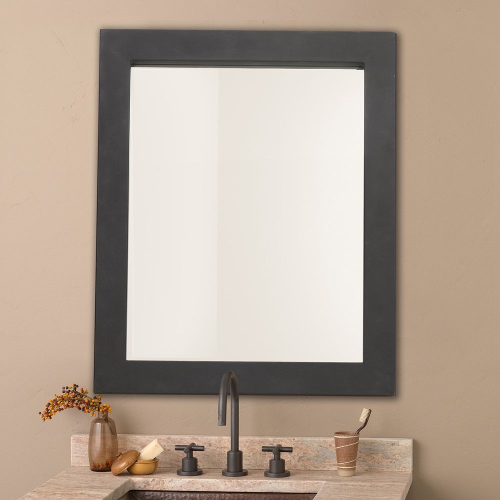 Rectangular mirror with dark gray frame mounted above bathroom sink countertop with faucet and accessories.