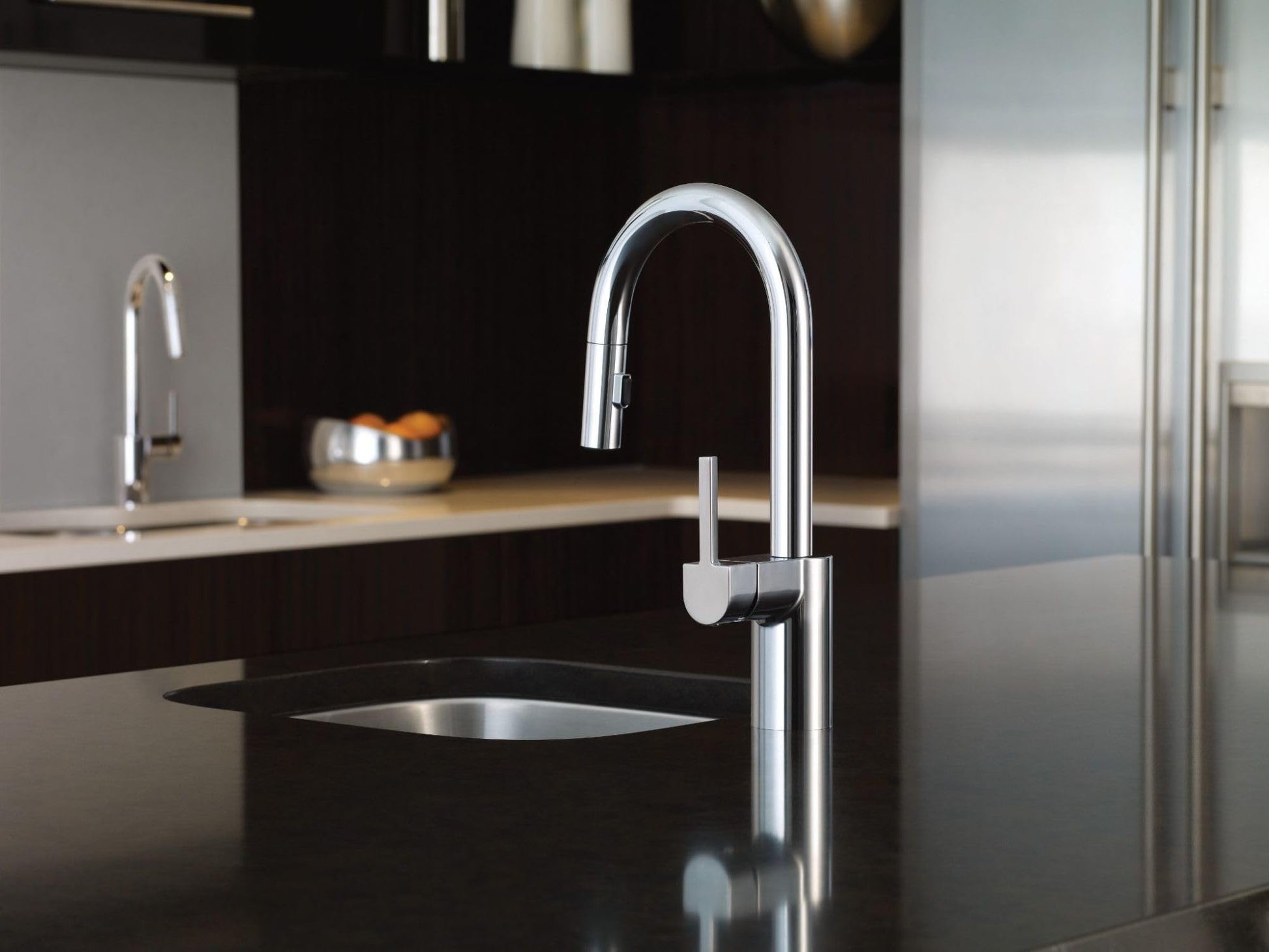 Chrome single-handle pulldown bar faucet with retractable spray head mounted on black countertop.