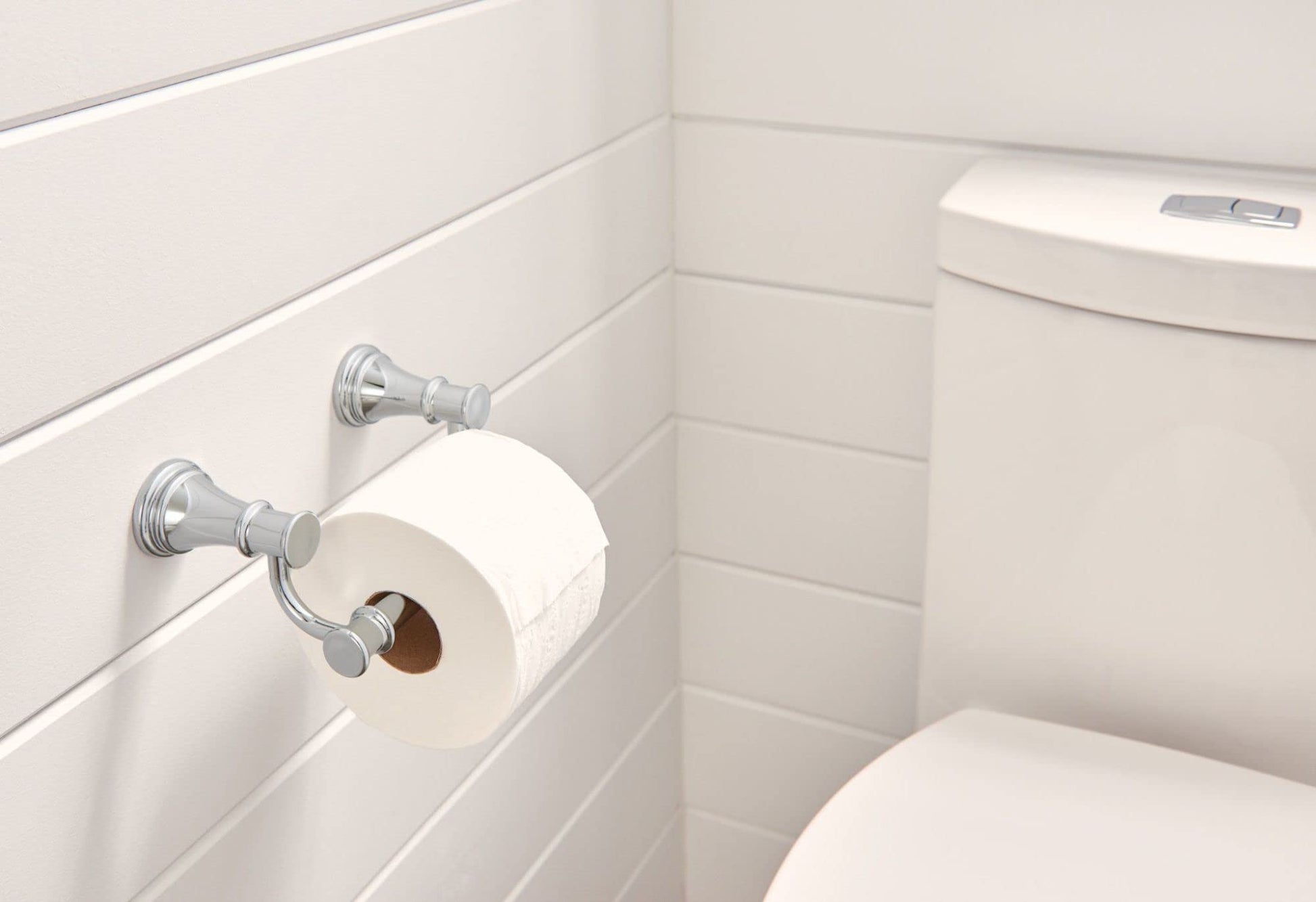 Chrome toilet paper holder mounted on white bathroom wall with roll installed.