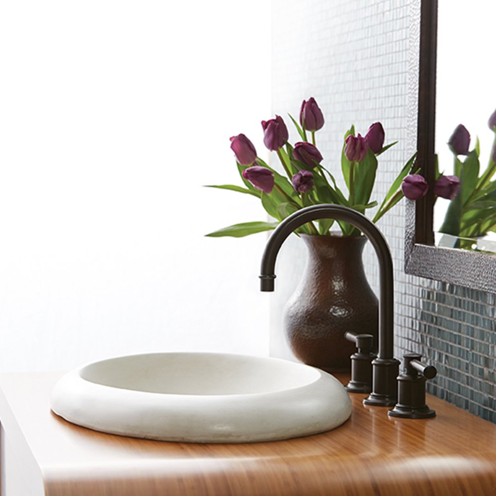 Pearl white round vessel sink with curved rim on wood countertop with bronze faucet.
